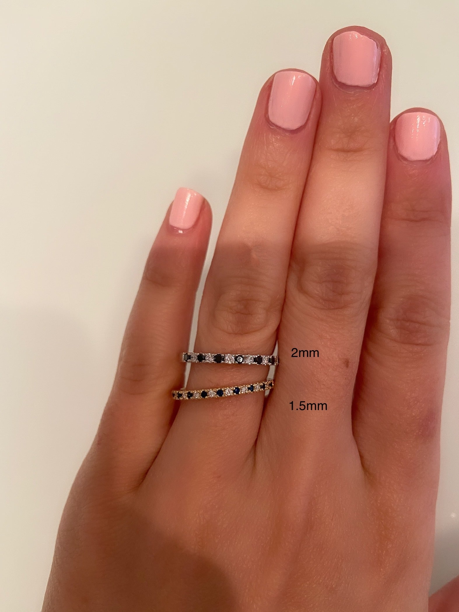 A comparison between a 2mm and 1.5mm alternating diamond and birthstone ring on a person's finger against a neutral background.