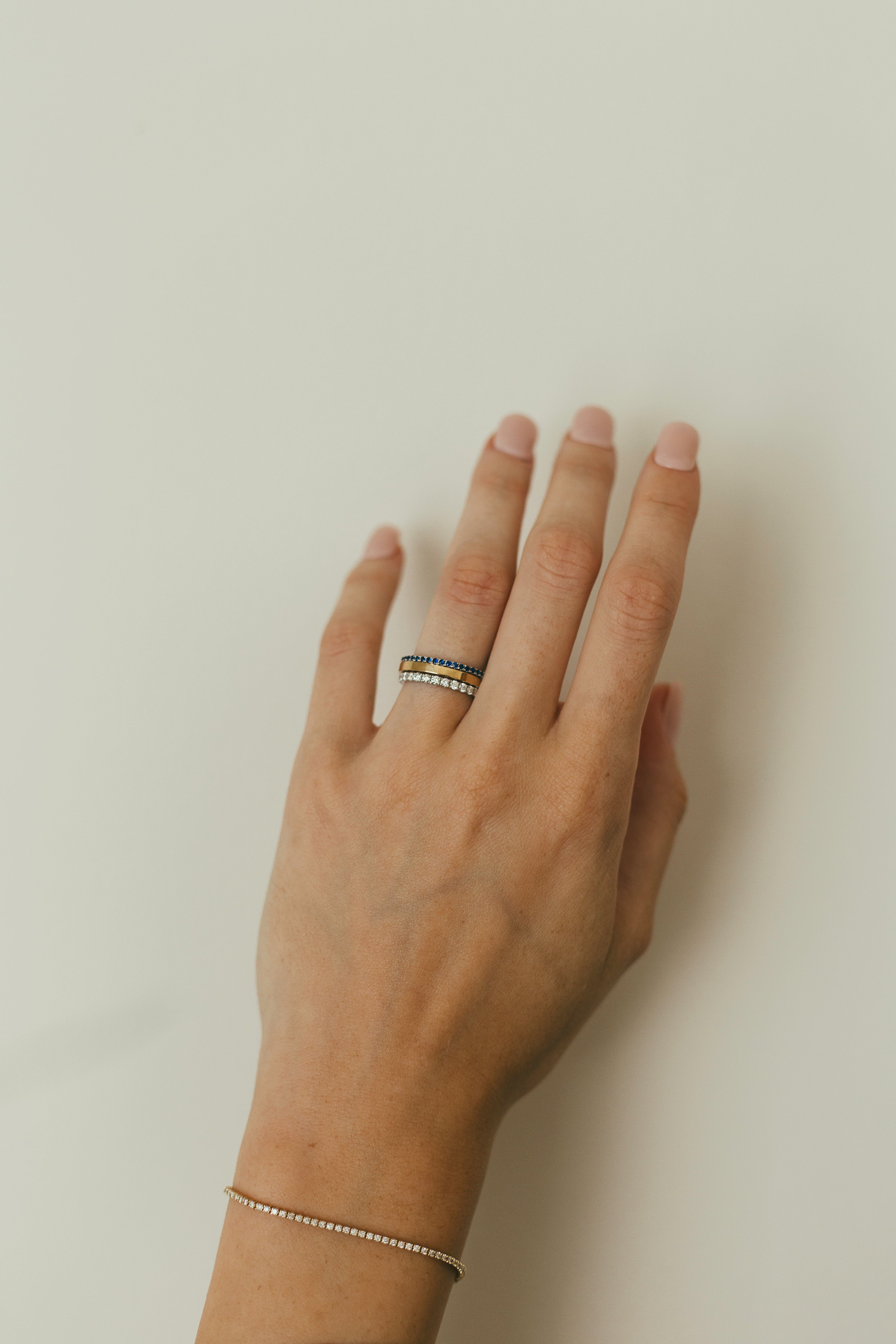 A person's hand styled with a stack of birthstone, gold, and diamond rings with a dainty tennis bracelet on the wrist
