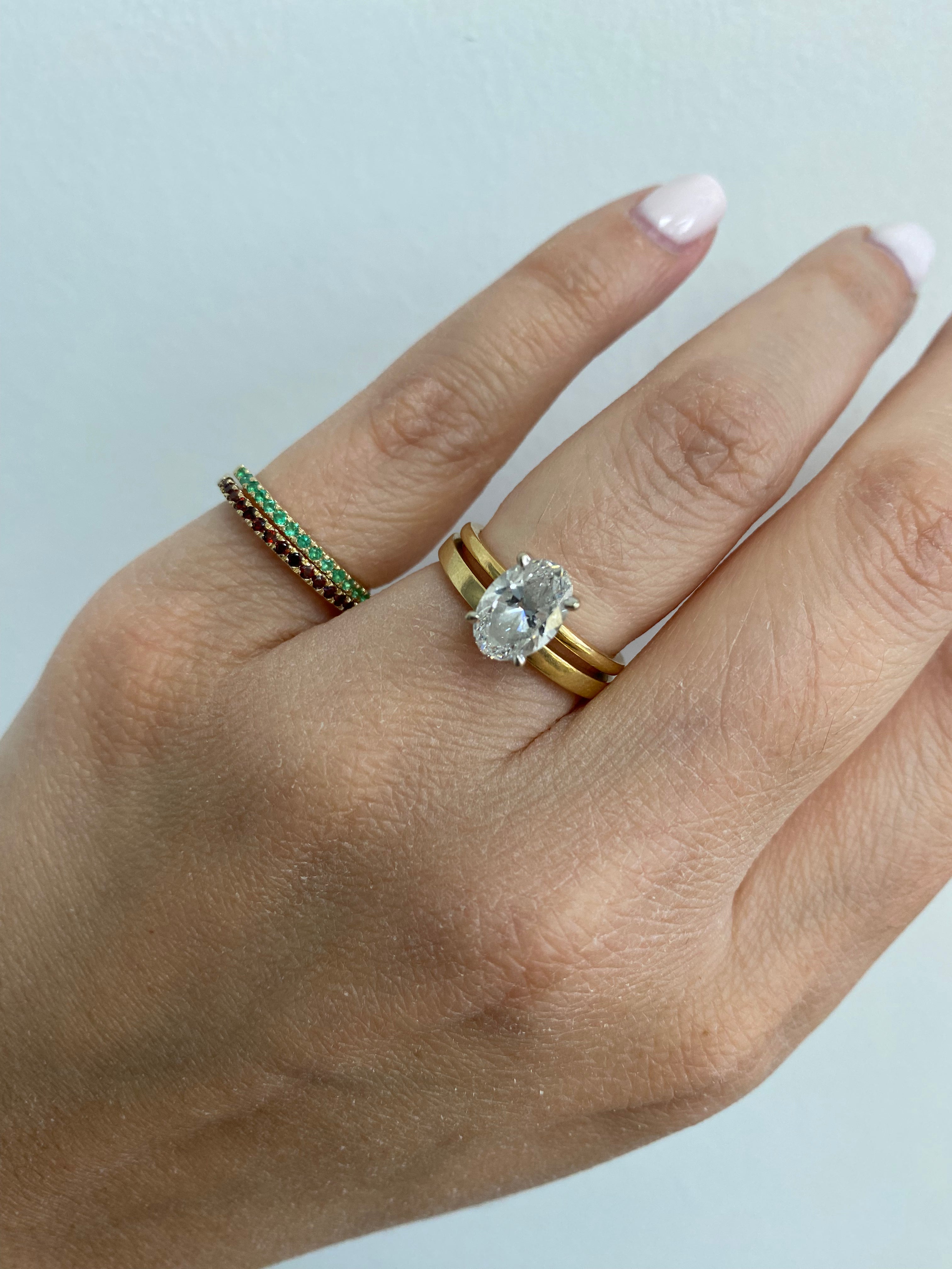 Close-up of a 1.5mm birthstone ring styled with other gold and diamond stacked rings on a person's hand.