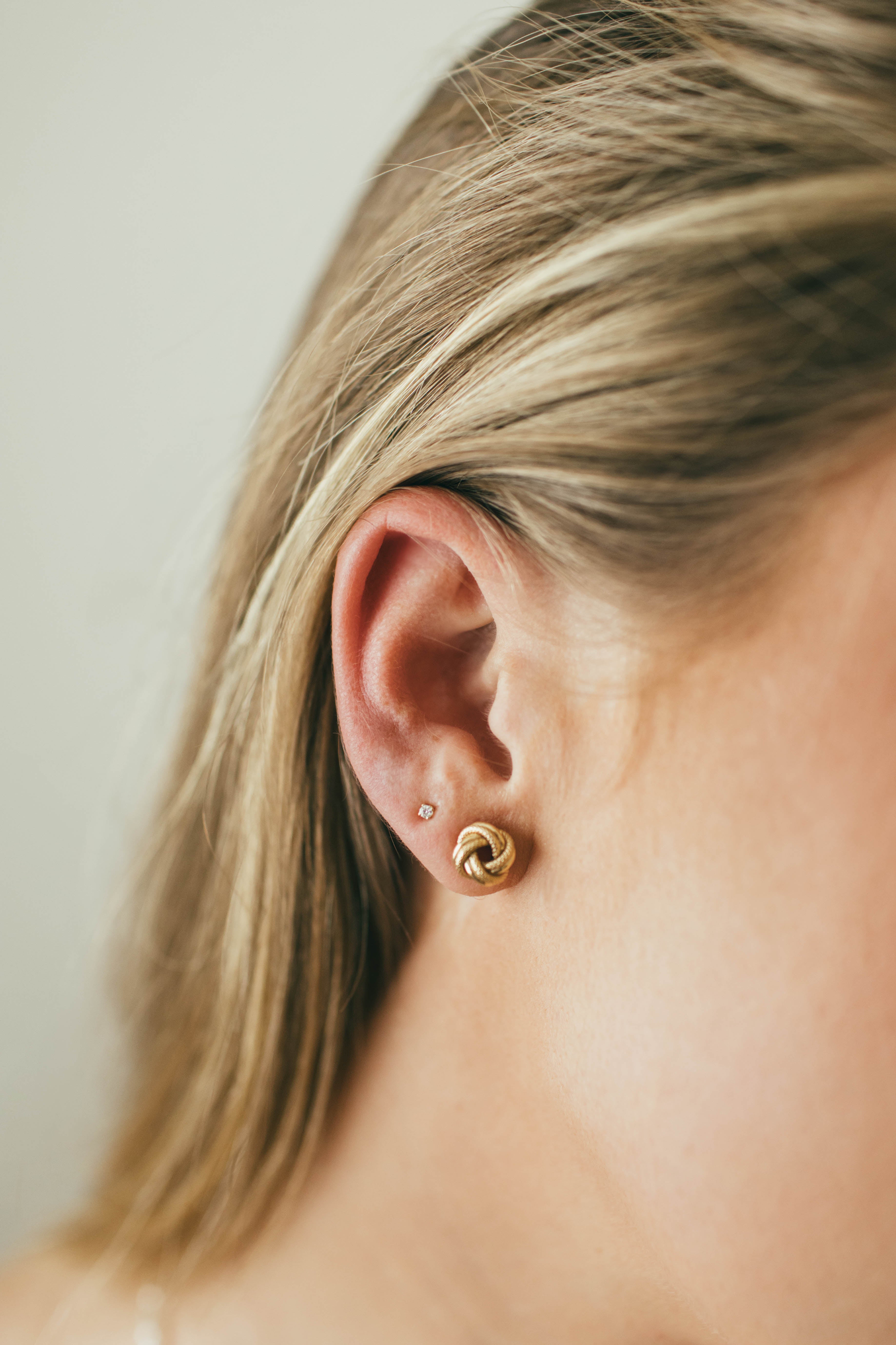 Close-up of a person wearing gold stud earrings with a neutral background