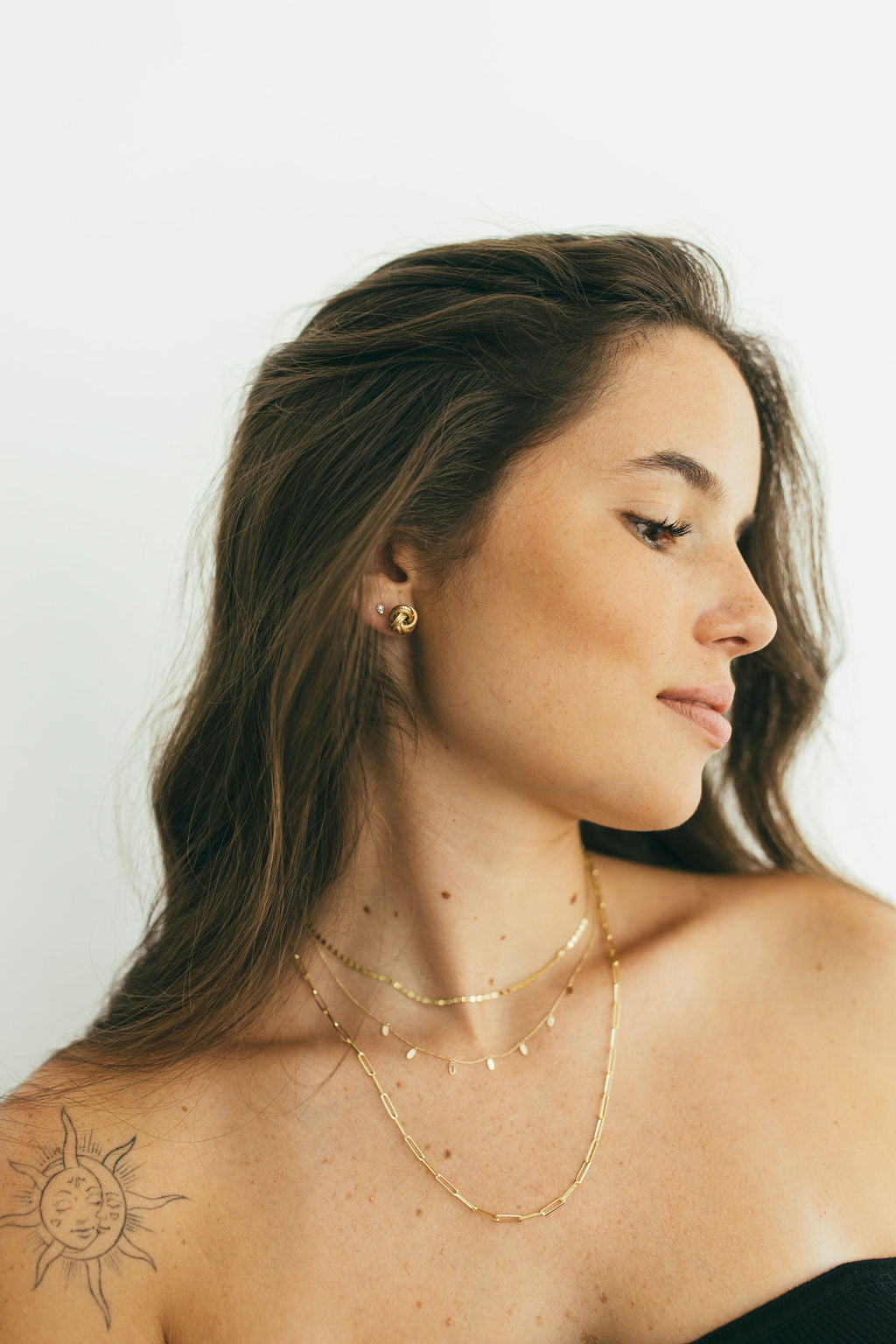 Woman wearing gold necklaces and earrings against a white background