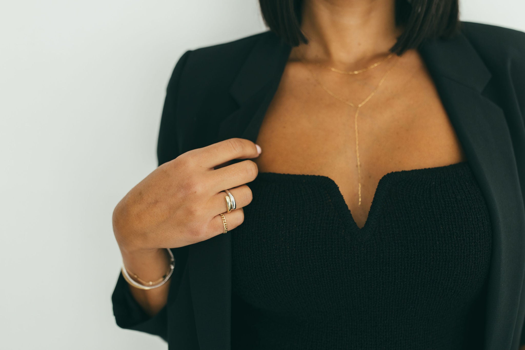 A chunky white and yellow gold wrap ring on a woman's hand styled with a black top and blazer against a neutral background.