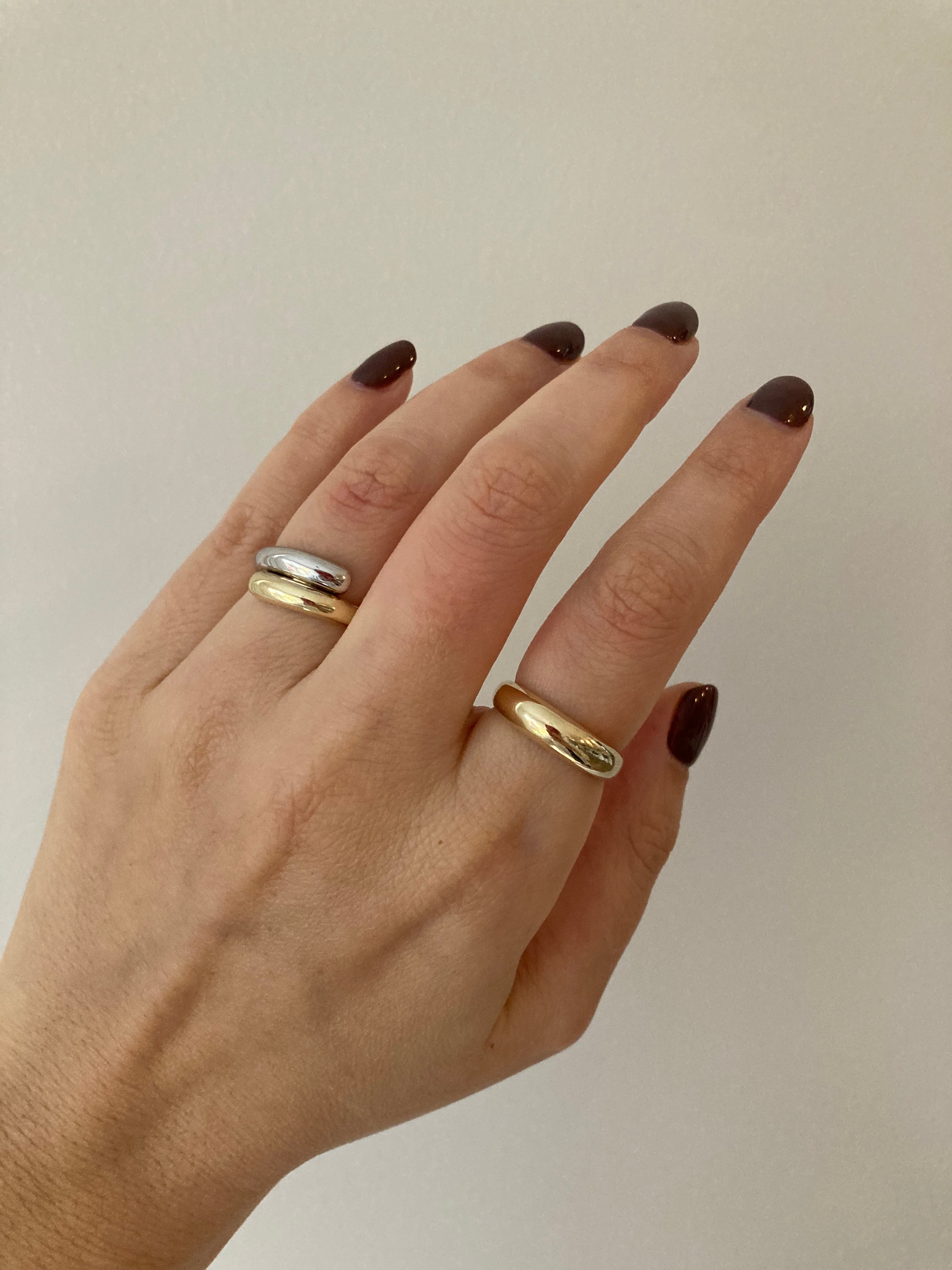 A chunky white and yellow gold wrap ring styled with a simple chunky yellow gold ring on a woman's hand.