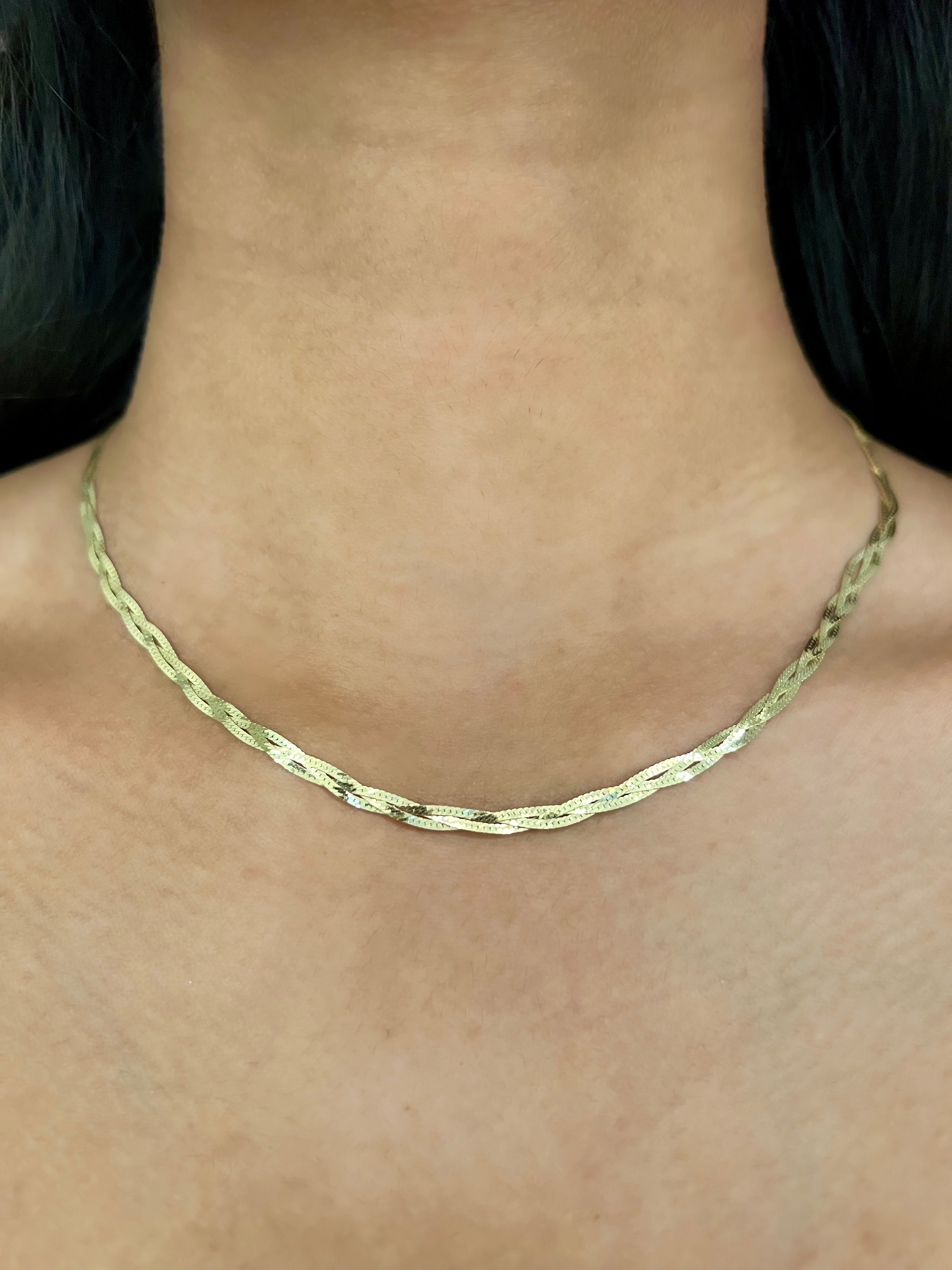 A close-up of a person's neck and upper chest wearing a gold braided herringbone necklace.