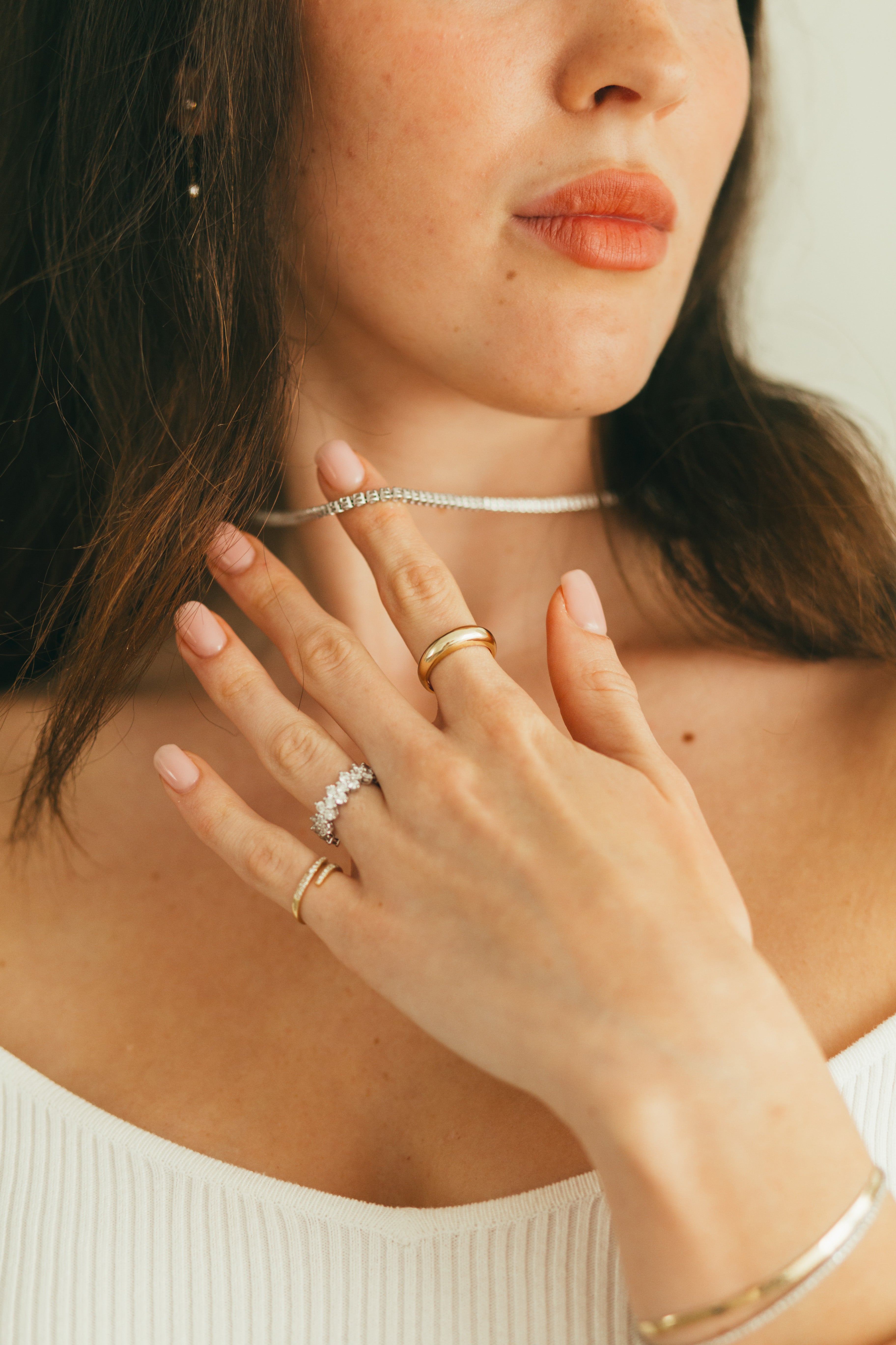 A close up of a woman wearing a mix of chunky gold rings and diamond rings with a diamond tennis necklace.