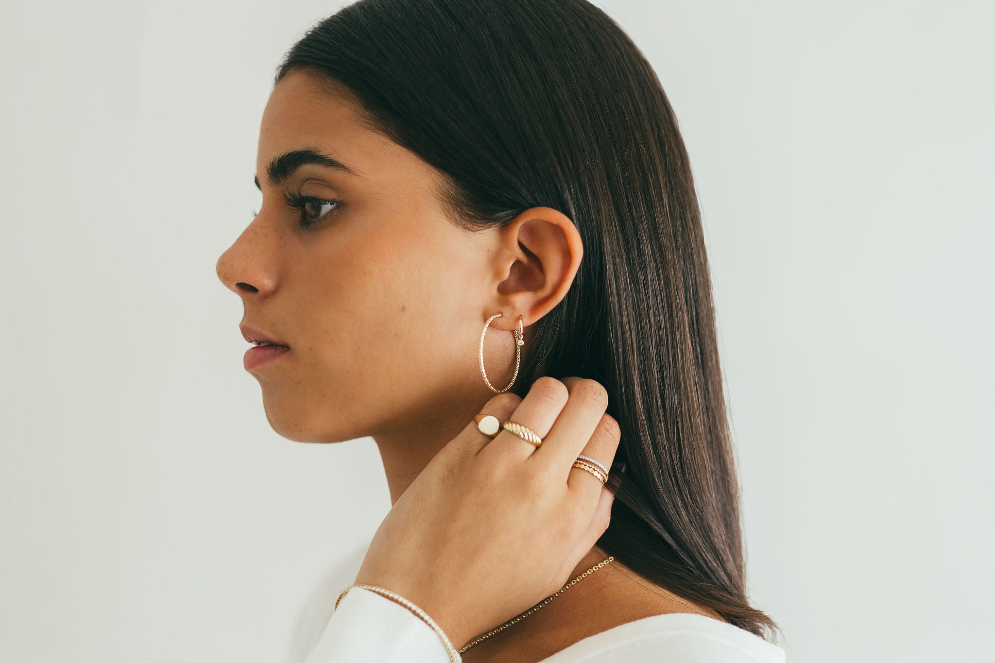 Woman wearing gold diamond-cut sparkle sleeper hoop earrings on a plain background.