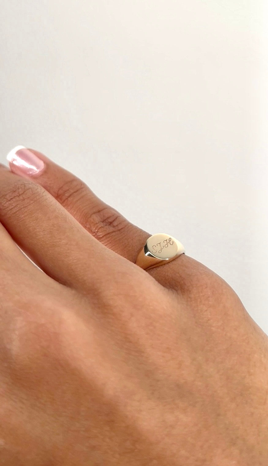 A close-up of a person's hand wearing a gold signet ring with three engraved initials.