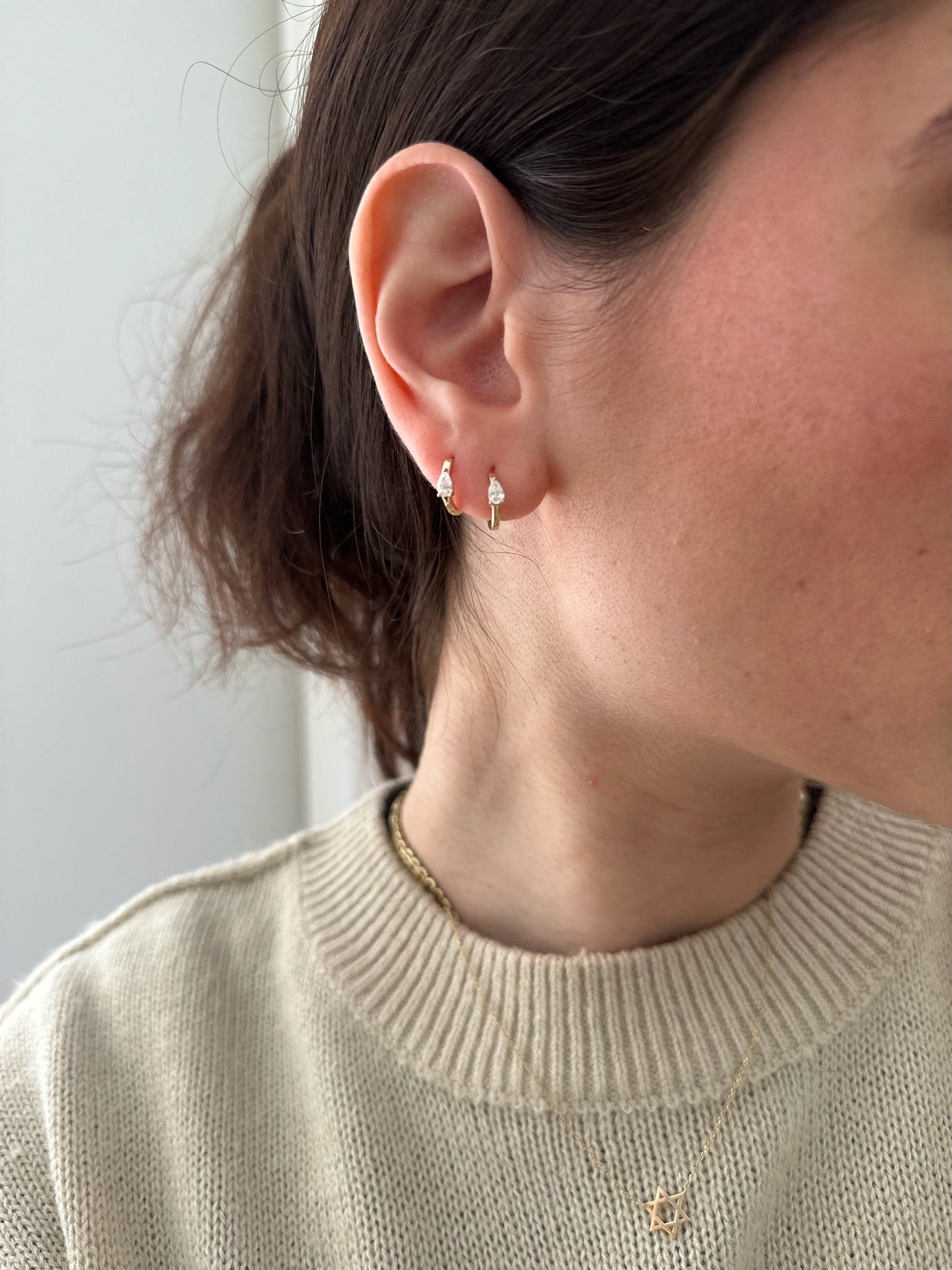 Close-up of a person wearing gold earrings and a matching necklace against a neutral background