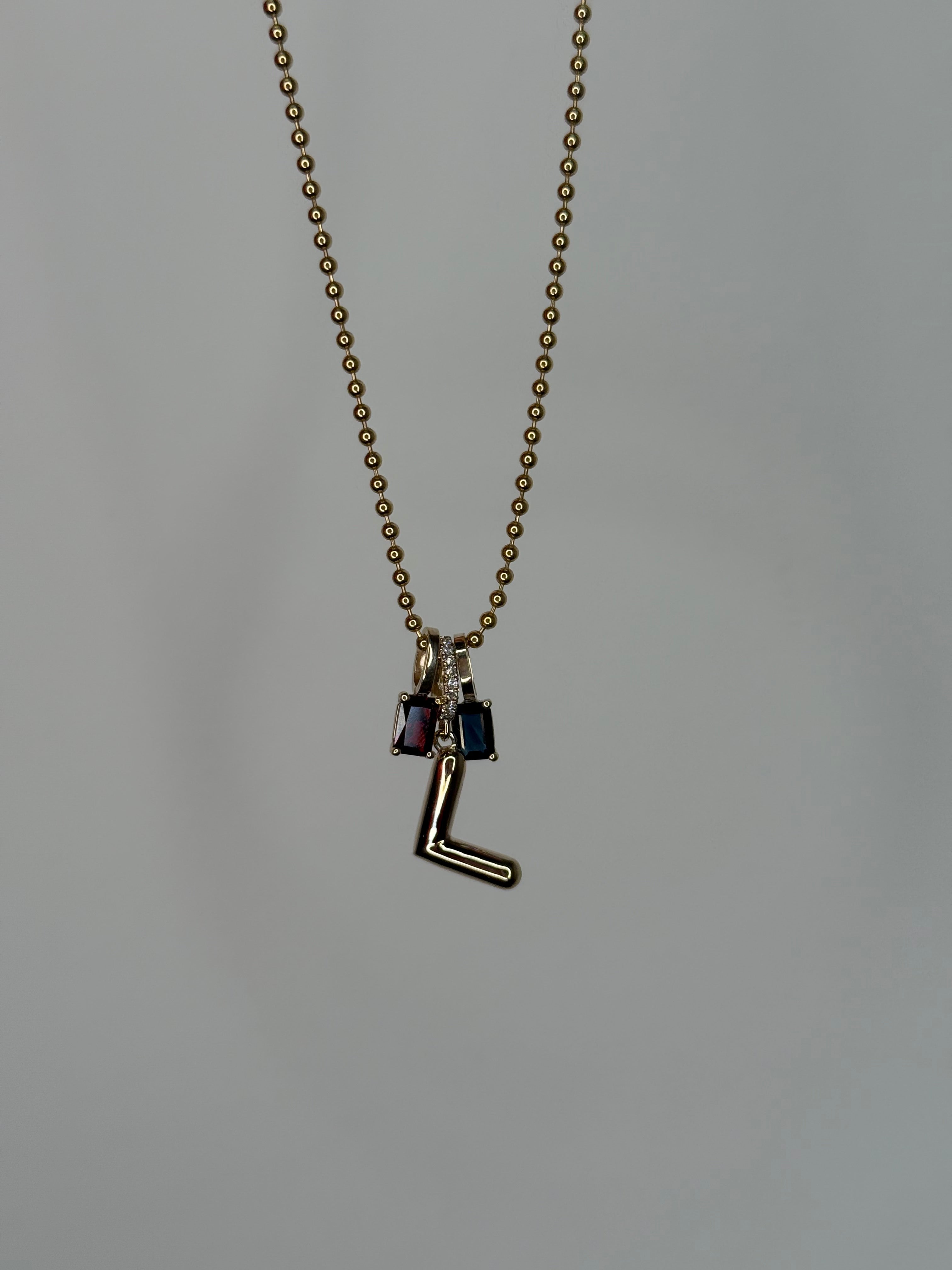 Gold necklace with an L pendant and two birthstone pendants on a plain background