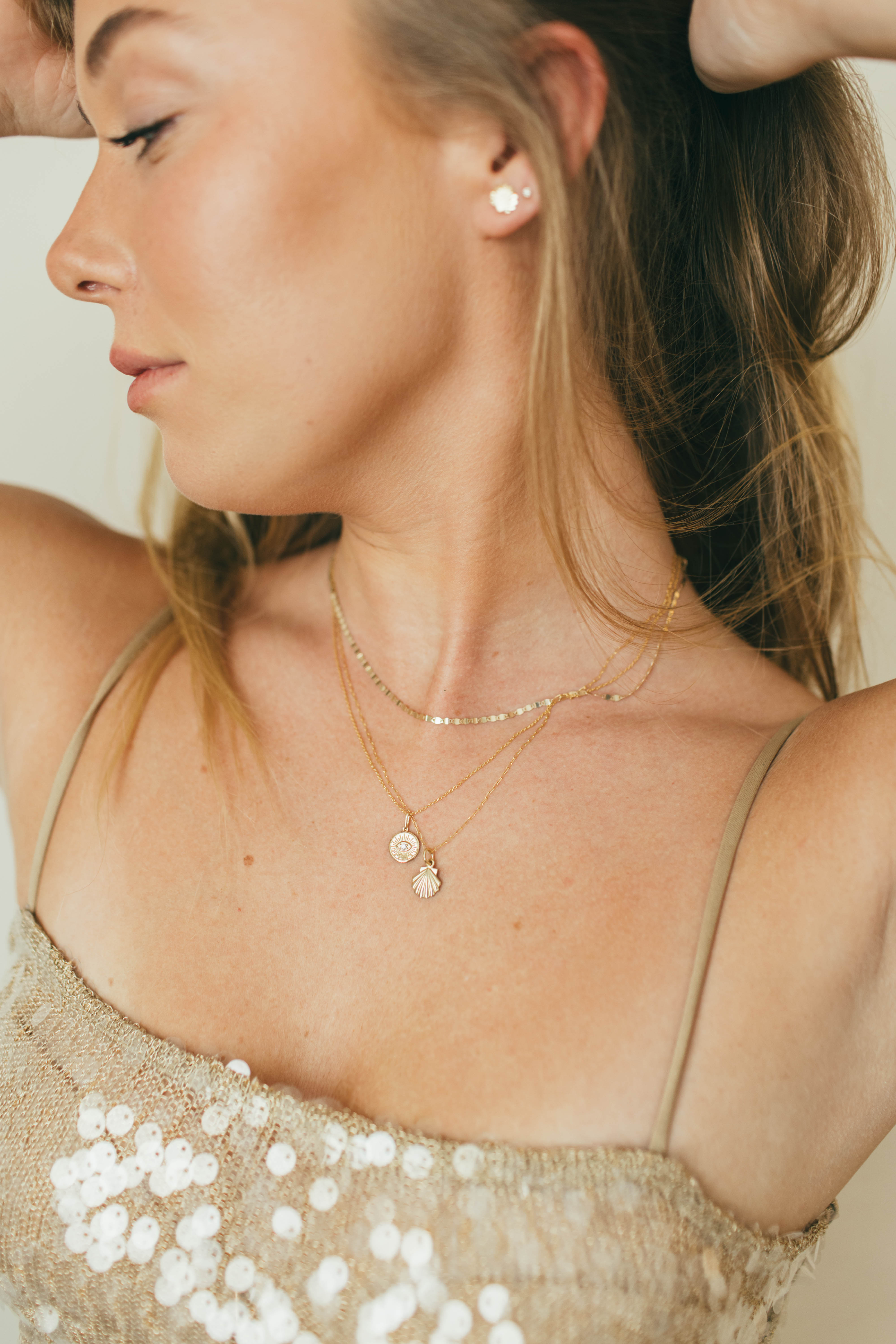 Close-up of a woman wearing gold necklaces and earrings with a neutral background