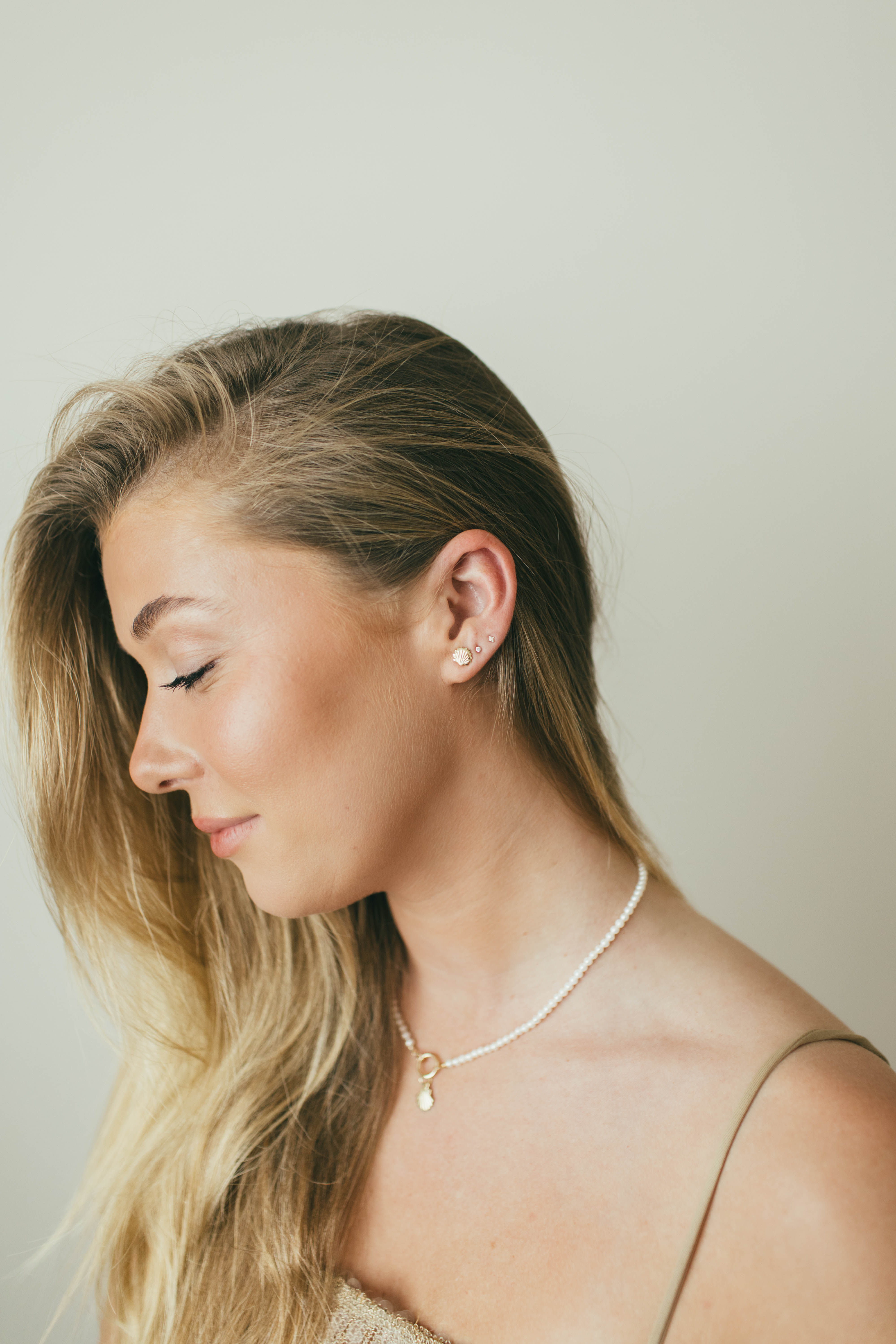 Woman wearing a delicate necklace and earring against a plain background