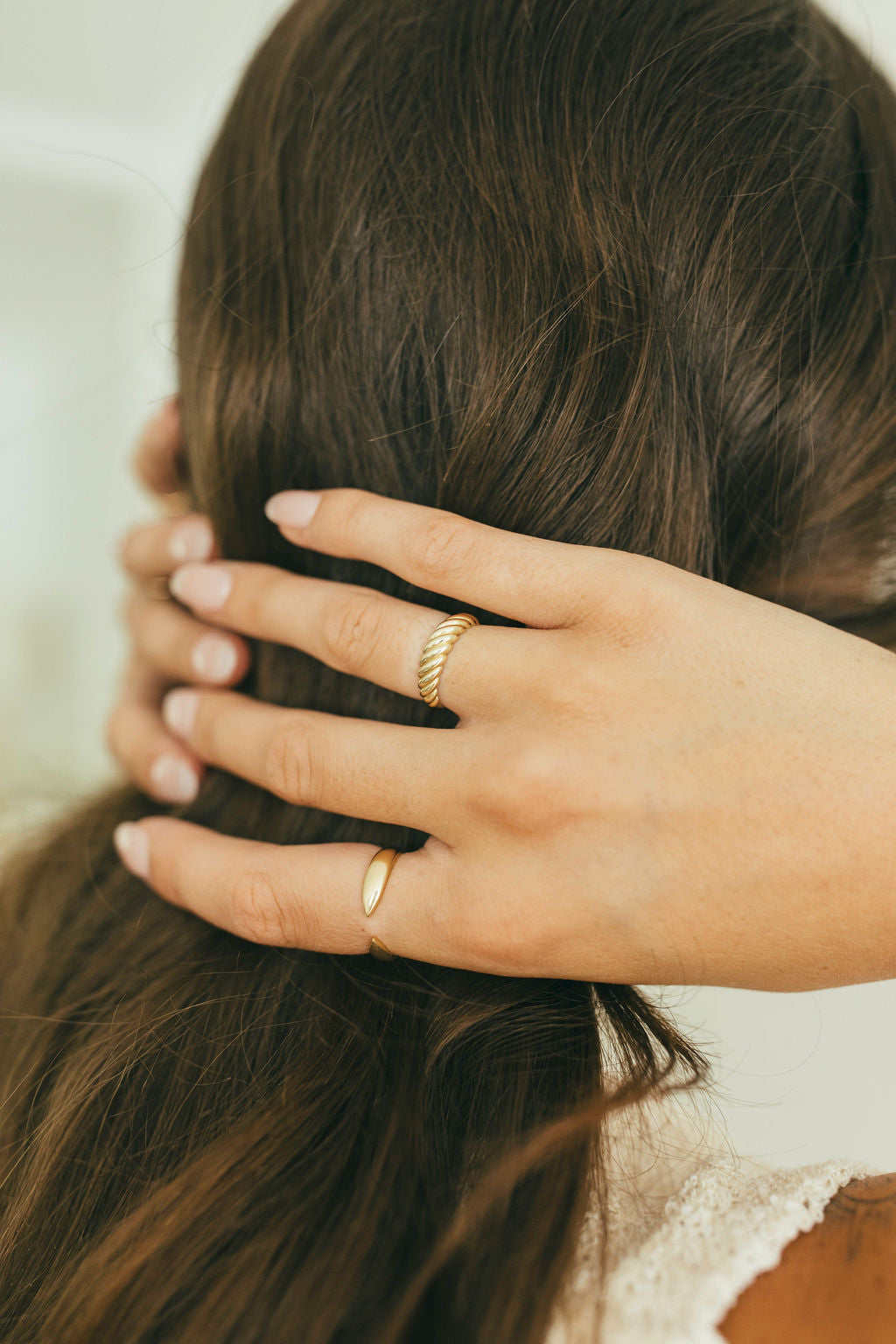 A woman holding her hair wearing yellow gold rings.