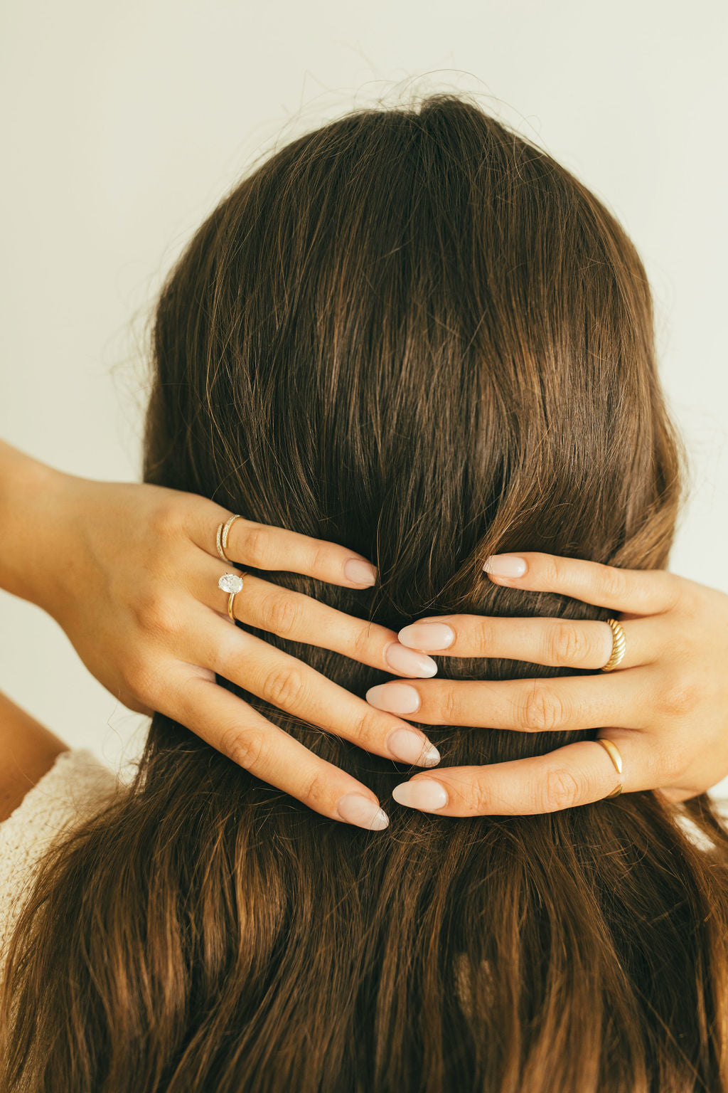 A woman with her hands in her hair, wearing different yellow gold rings.