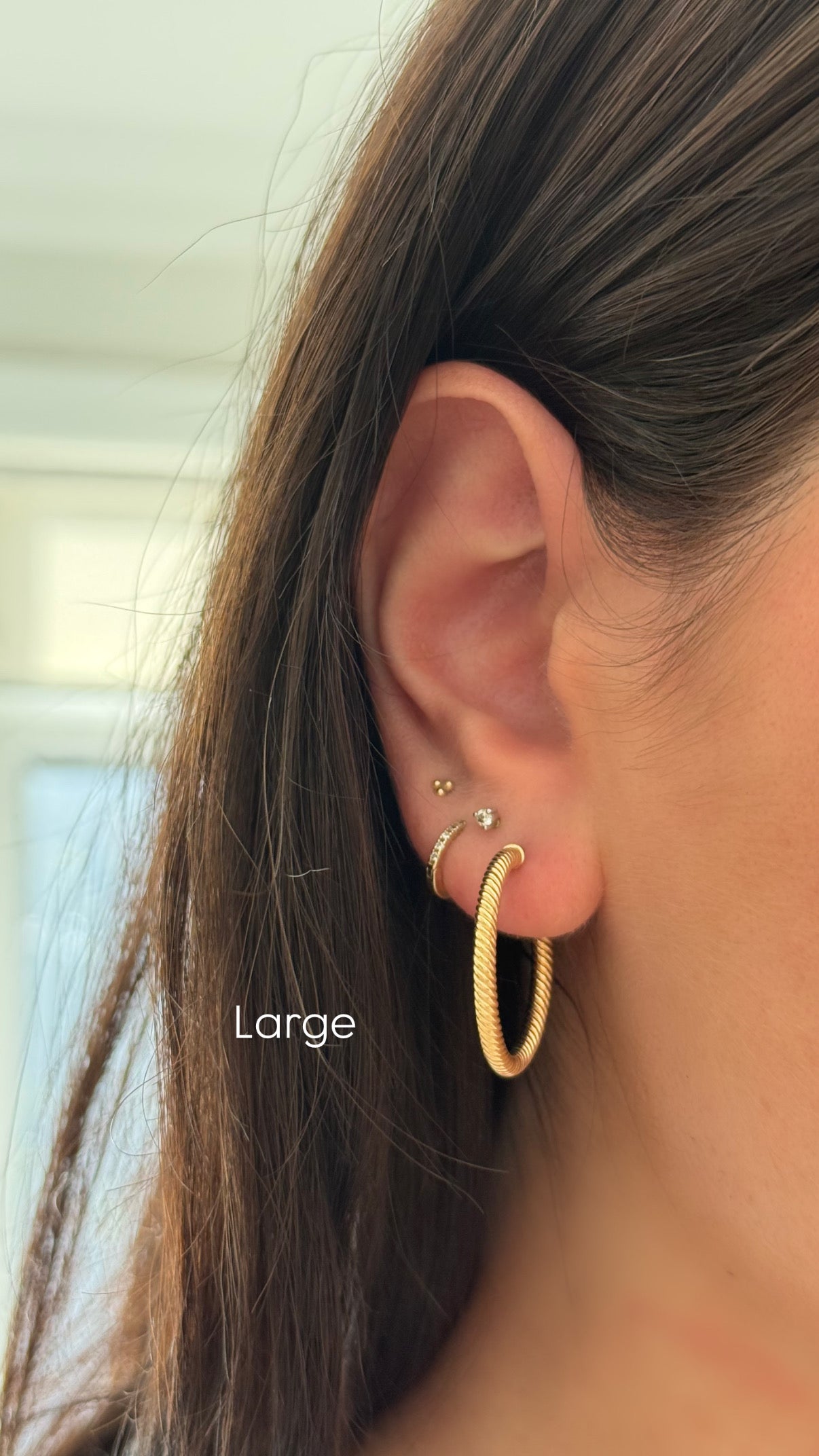 Gold hoop earring worn by a person with long hair, labeled 'Large'.