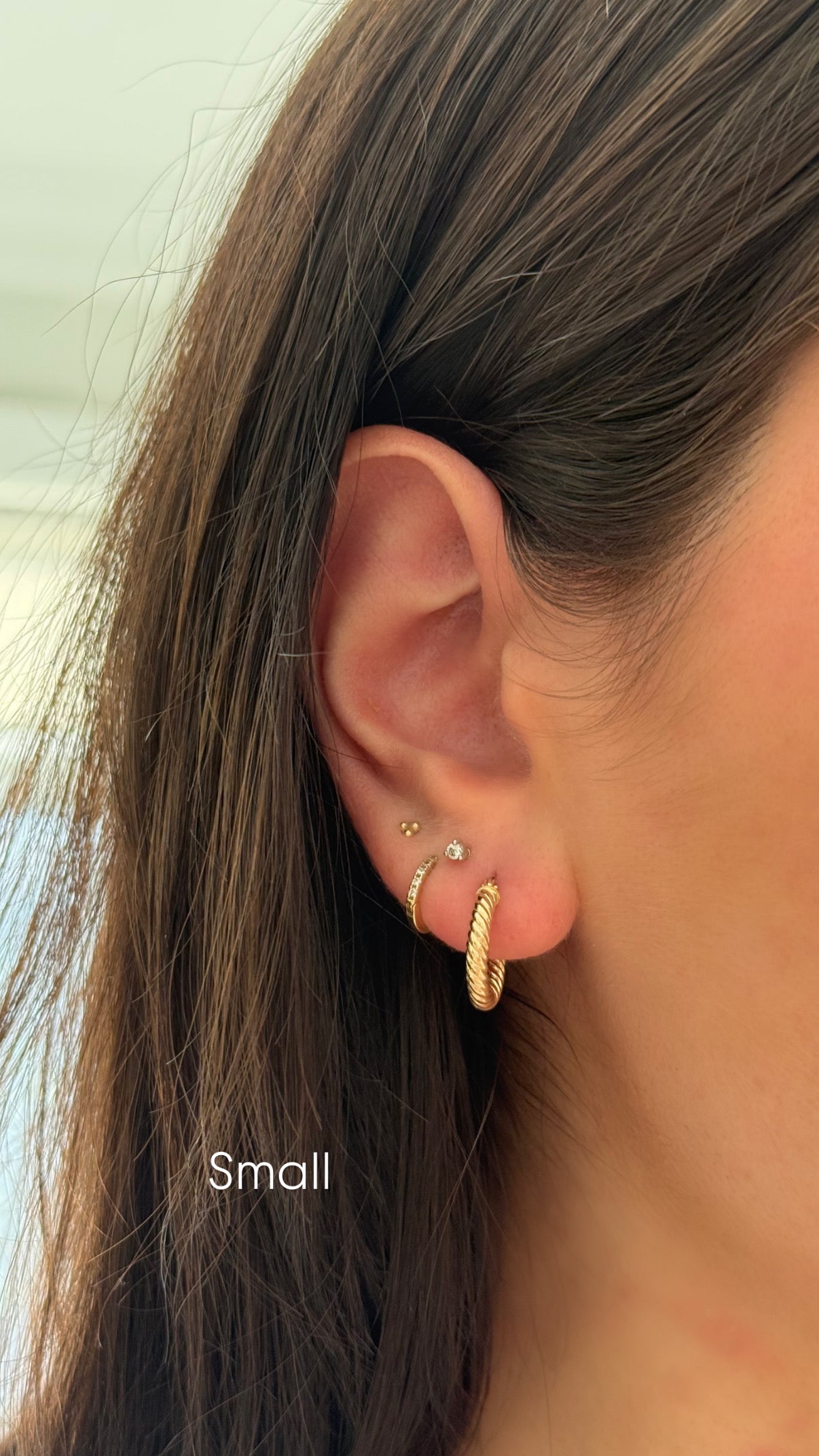Close-up of an ear wearing a gold hoop earring with 'Small' label.