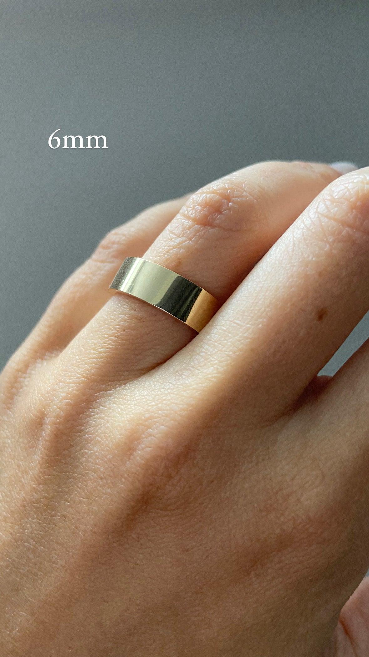 A close up of a hand styled with a single gold wide flat cigar band on a neutral background, with text indicating a "6mm" ring width.