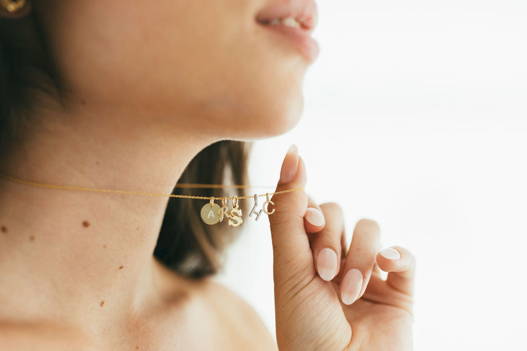 Close-up of a person wearing a gold necklace with initial pendants.