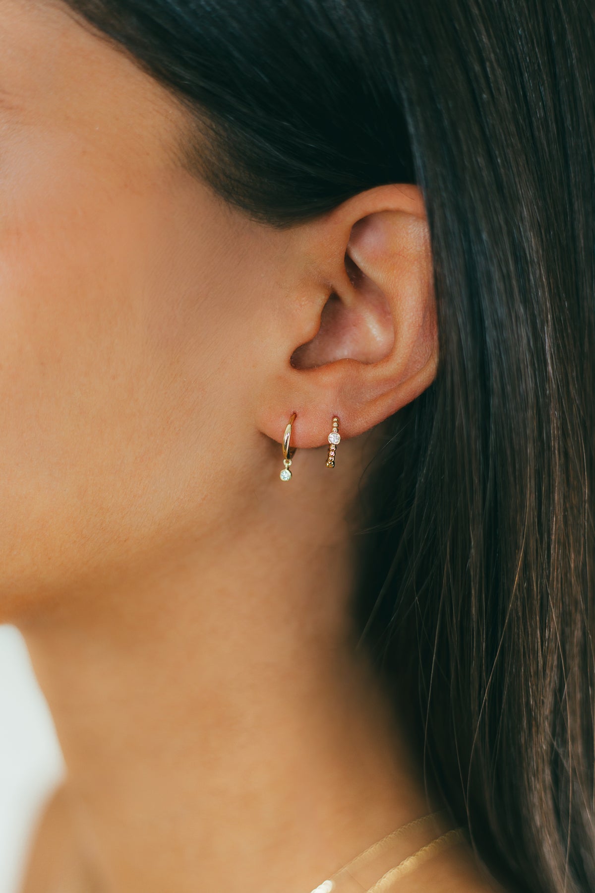 Close-up of a person wearing gold hoop earrings with small diamonds.