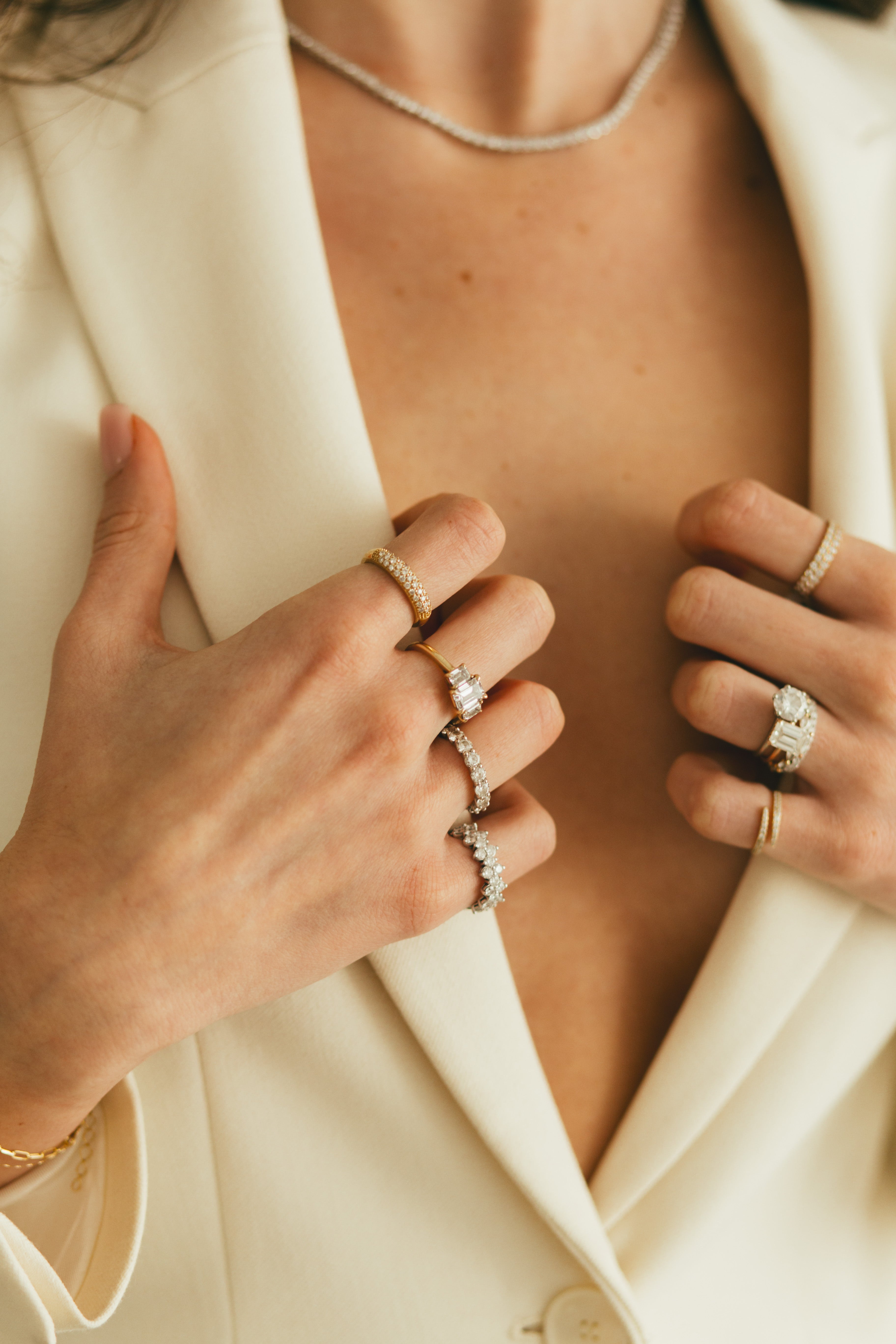 A woman holding her blazer accessorized with sparkling diamond rings.