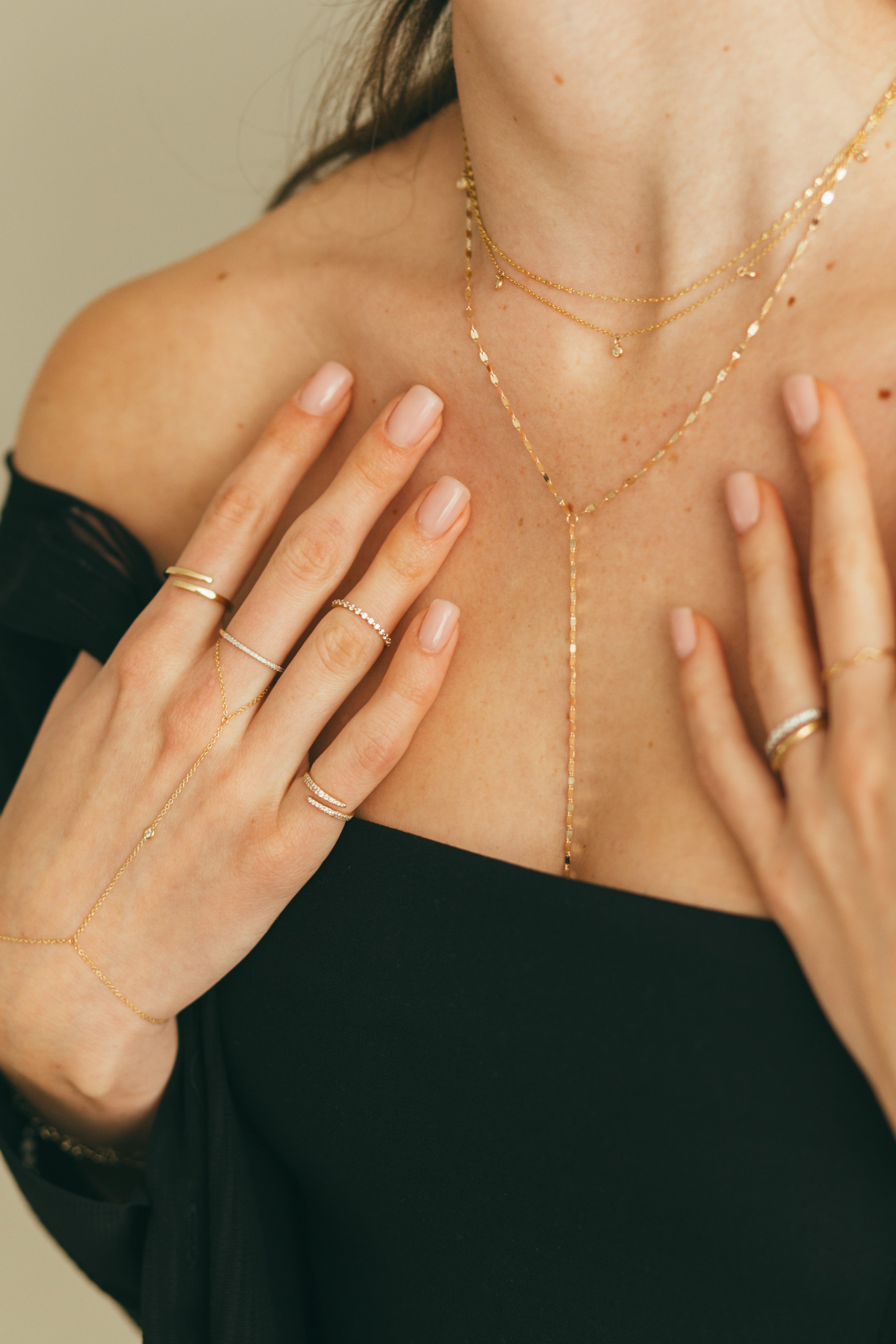 A person wearing a black off-shoulder top showcasing a 14K gold diamond hand chain that drapes elegantly across the hand with shimmering diamonds.