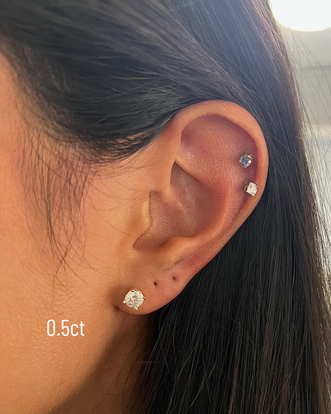 Close-up of an ear wearing a diamond stud earring with '0.5ct' label.