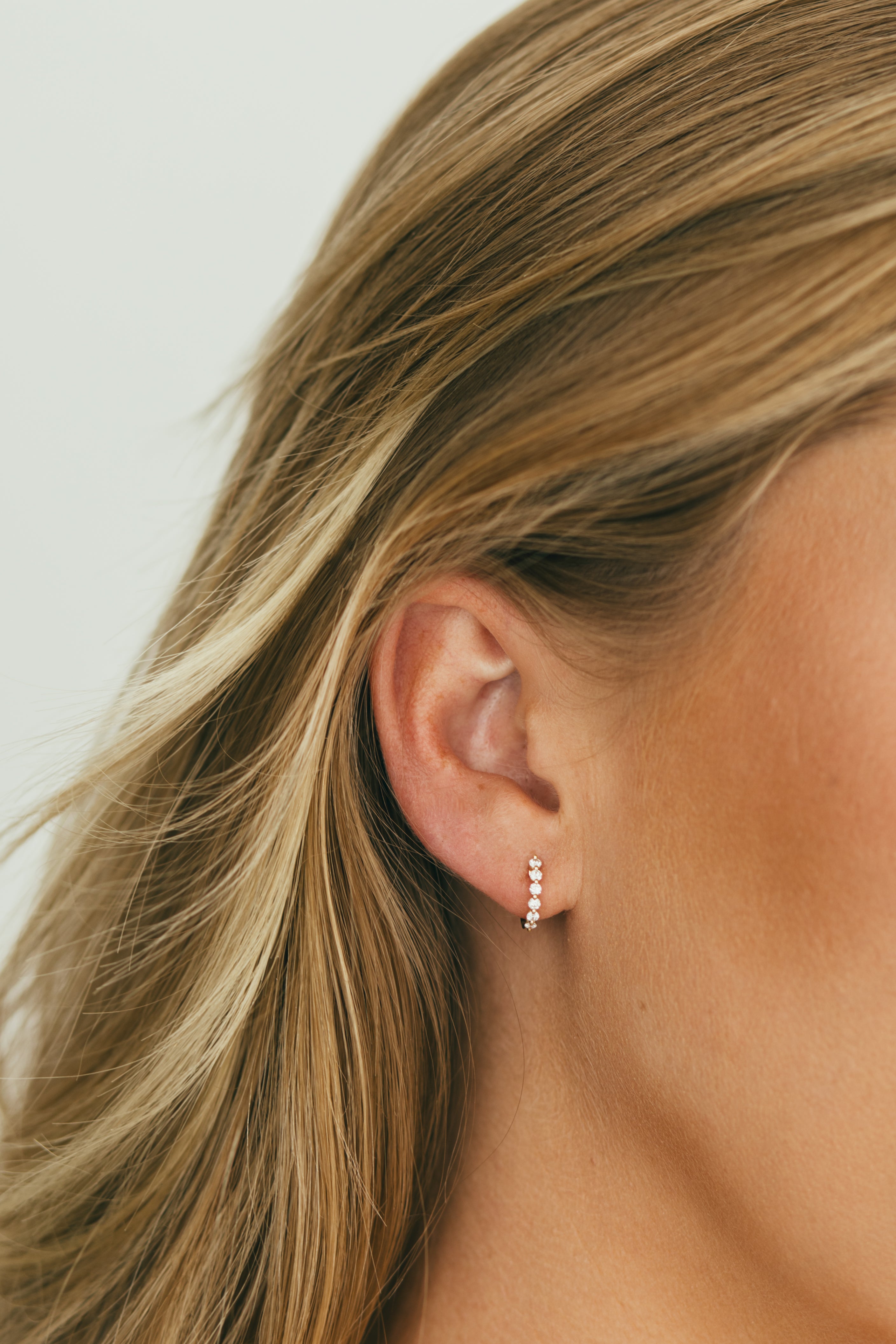 close up of girls ear wearing single prong diamond huggies