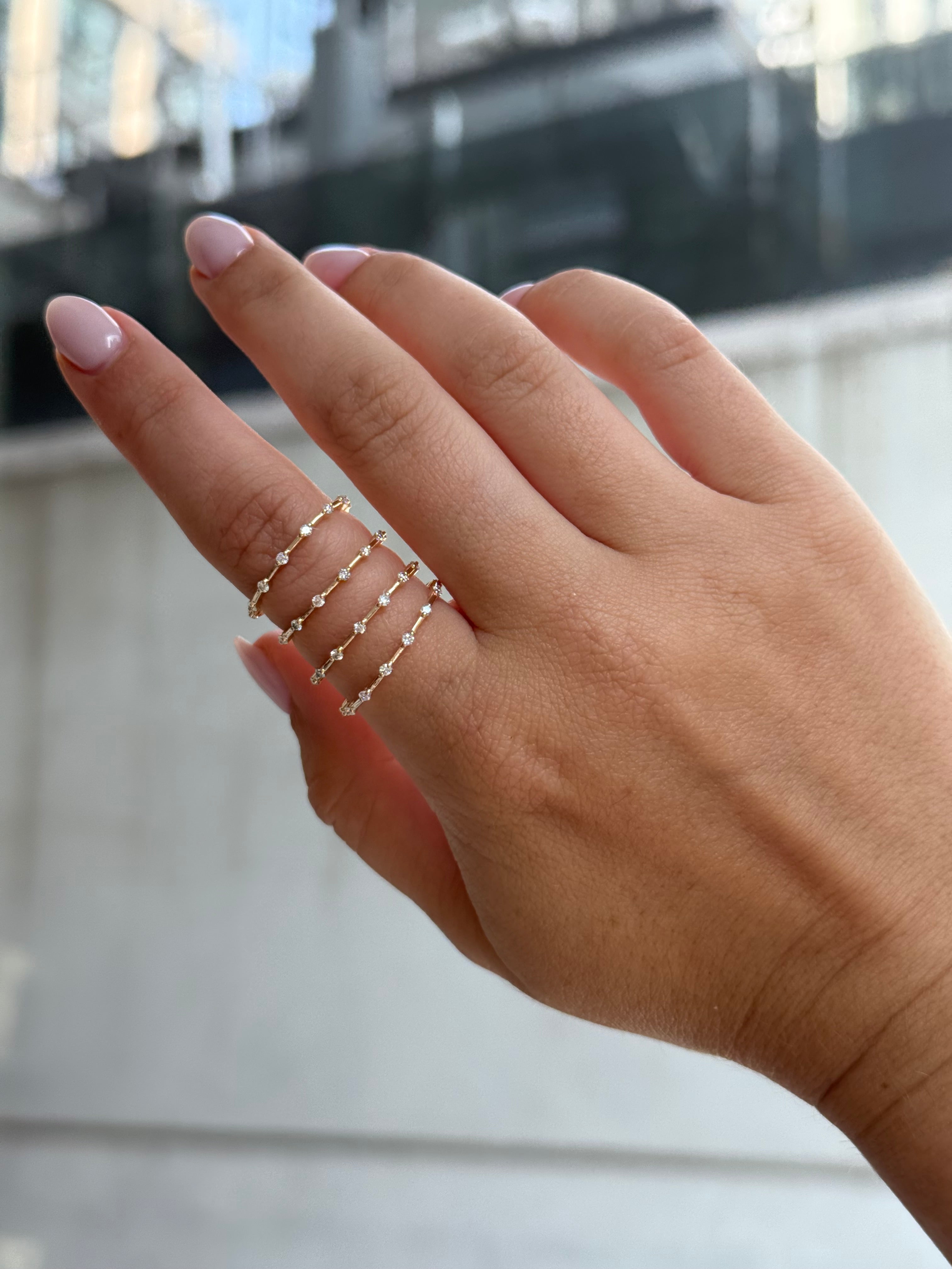 Hand wearing multiple gold spaced diamond rings with a blurred background.