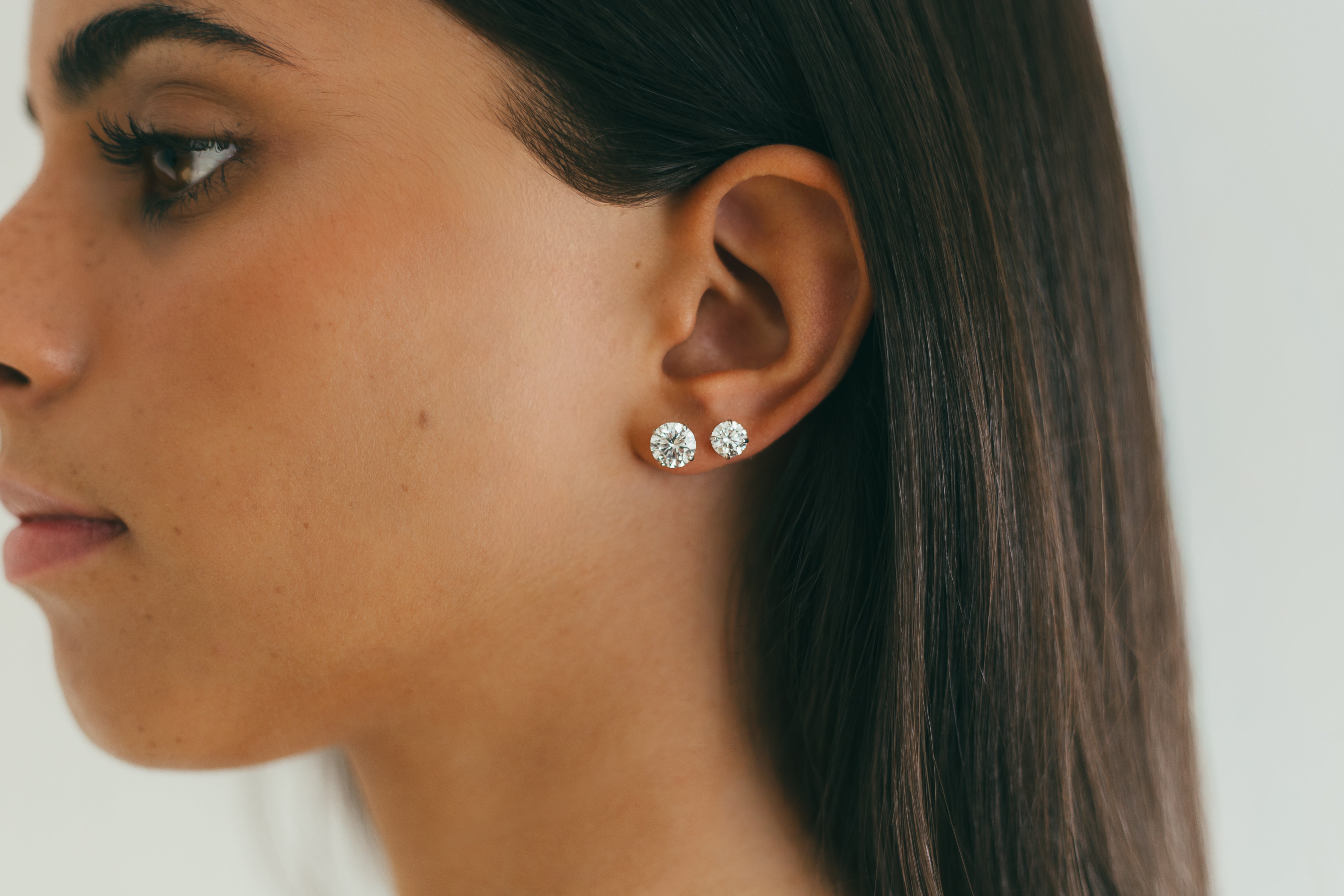 Close-up of a woman wearing diamond stud earrings with a neutral background