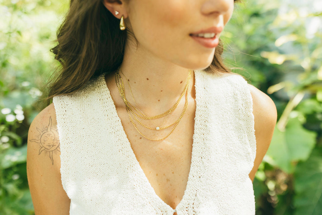 Woman wearing gold necklaces and earrings with a blurred green background