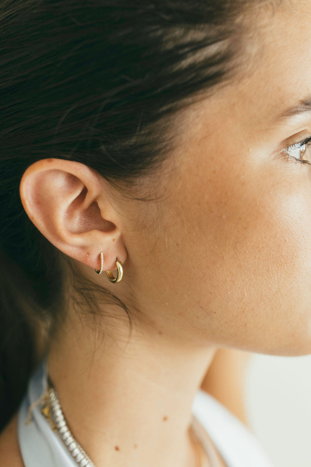 Close-up of a person wearing gold hoop earrings and pave diamond huggies