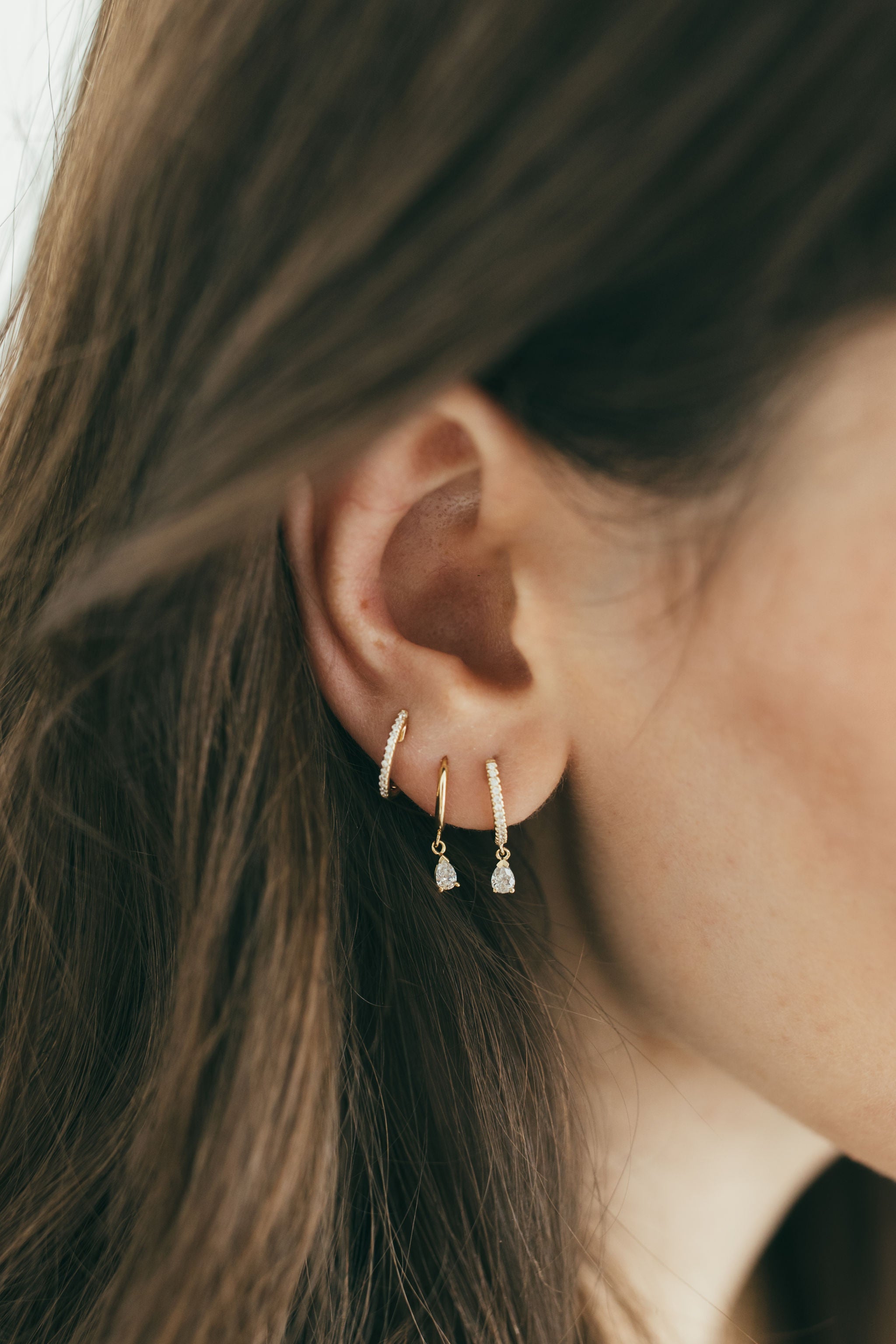 close up of girls ear wearing dangling diamond huggies and pave diamond huggie