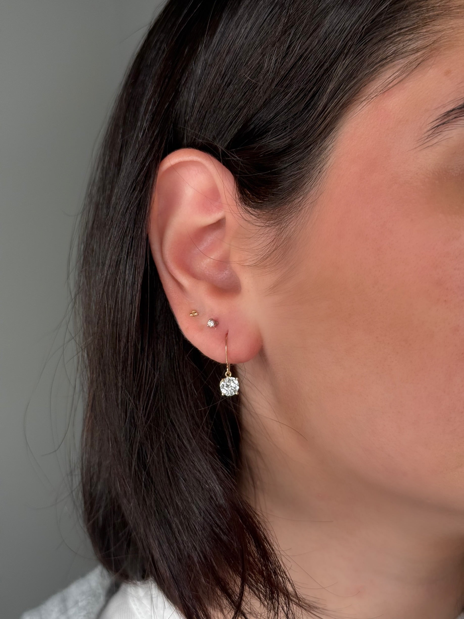 Close-up of a person wearing a diamond earring with a plain background