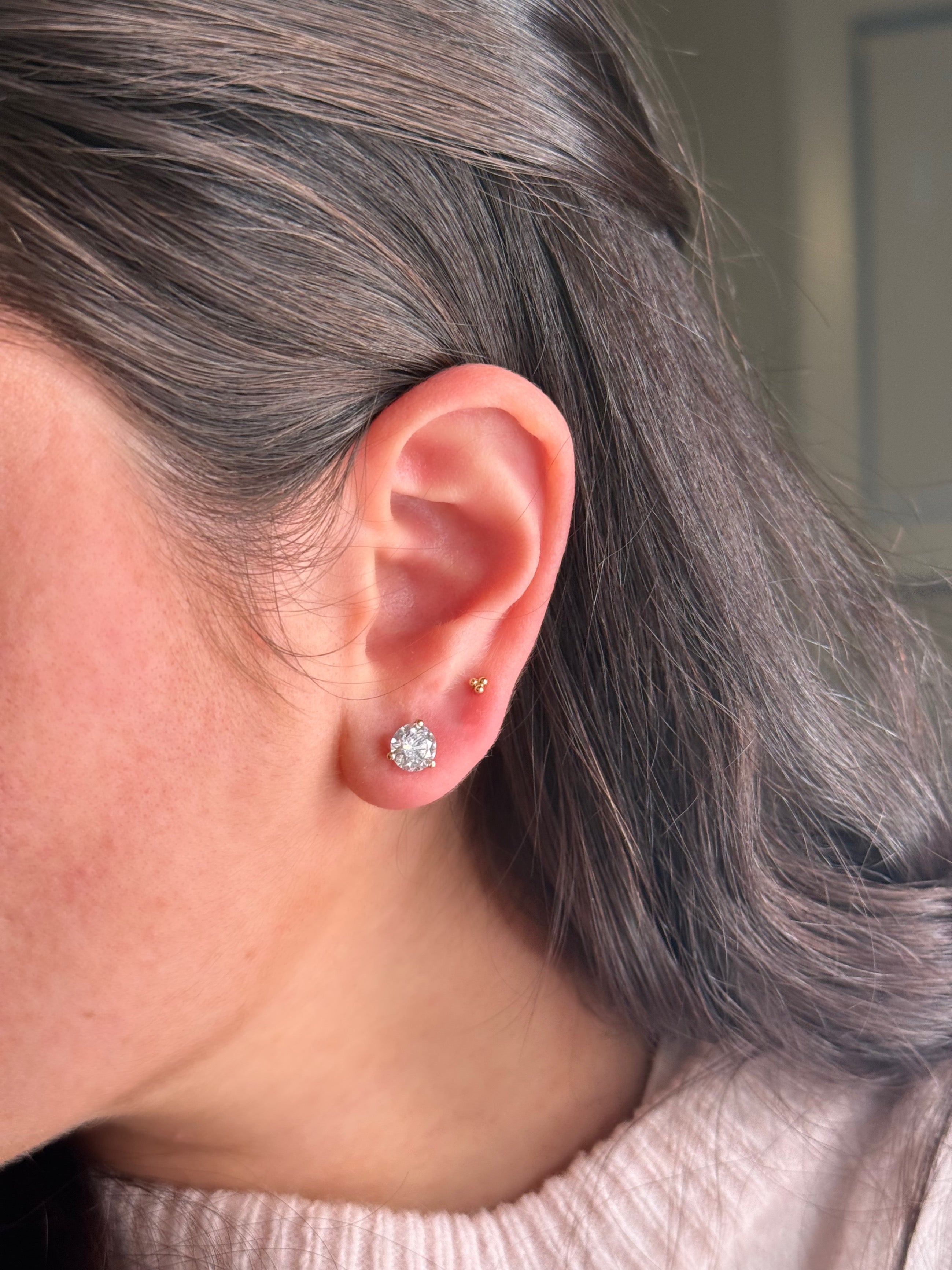 Close-up of a person wearing a diamond stud earring with a neutral background