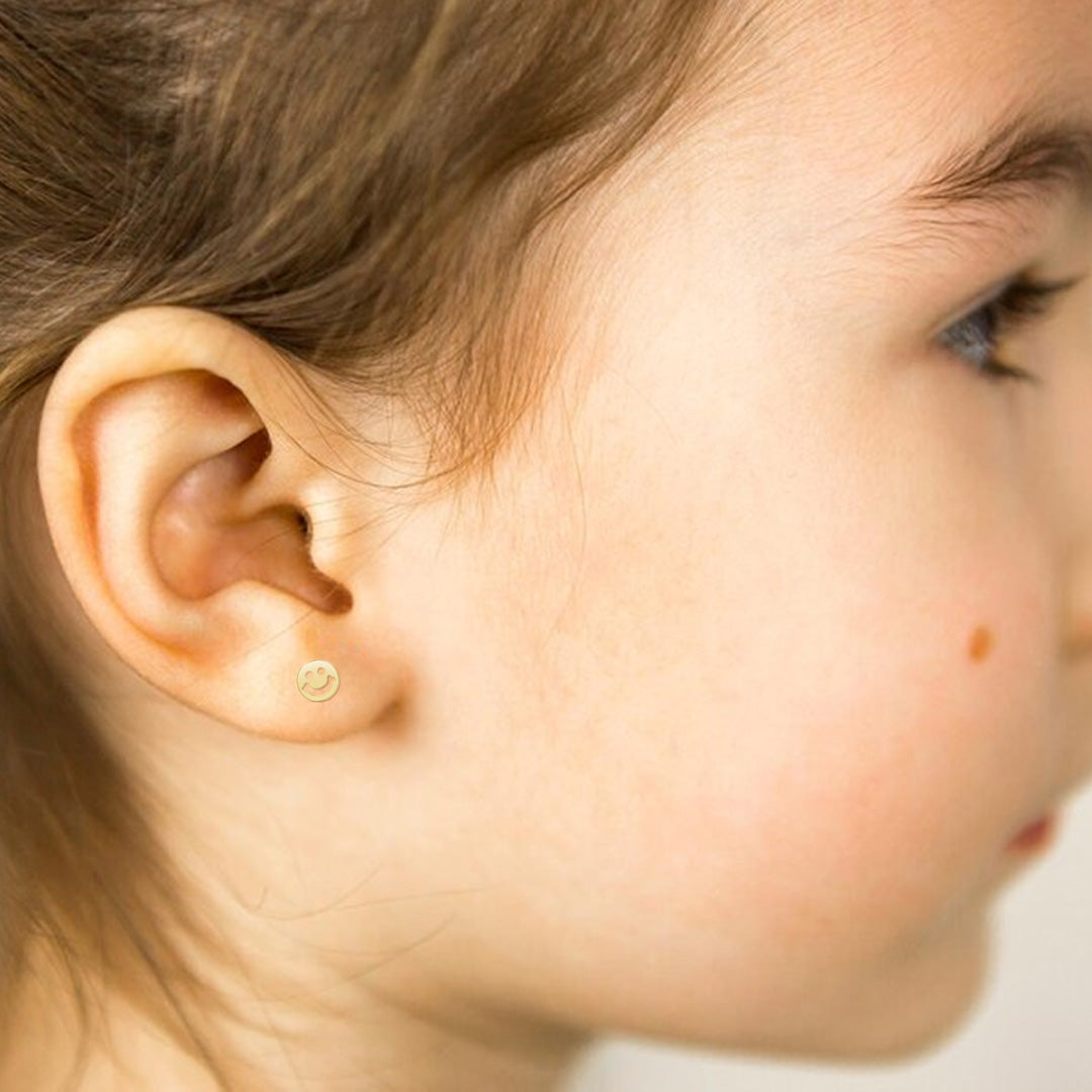 close up of little girls ears wearing gold happy face studs