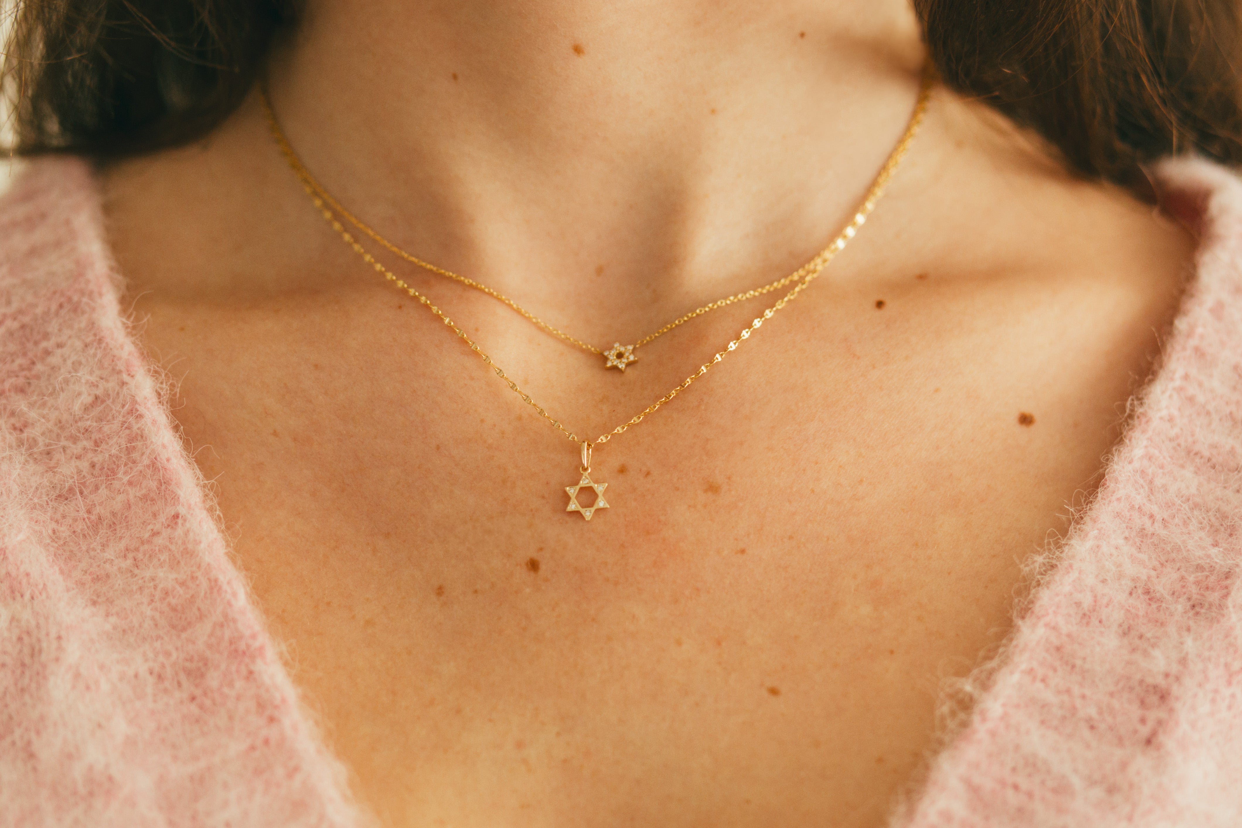 close up of mini diamond star of david necklace and open diamond star of david pendant on a gold chain