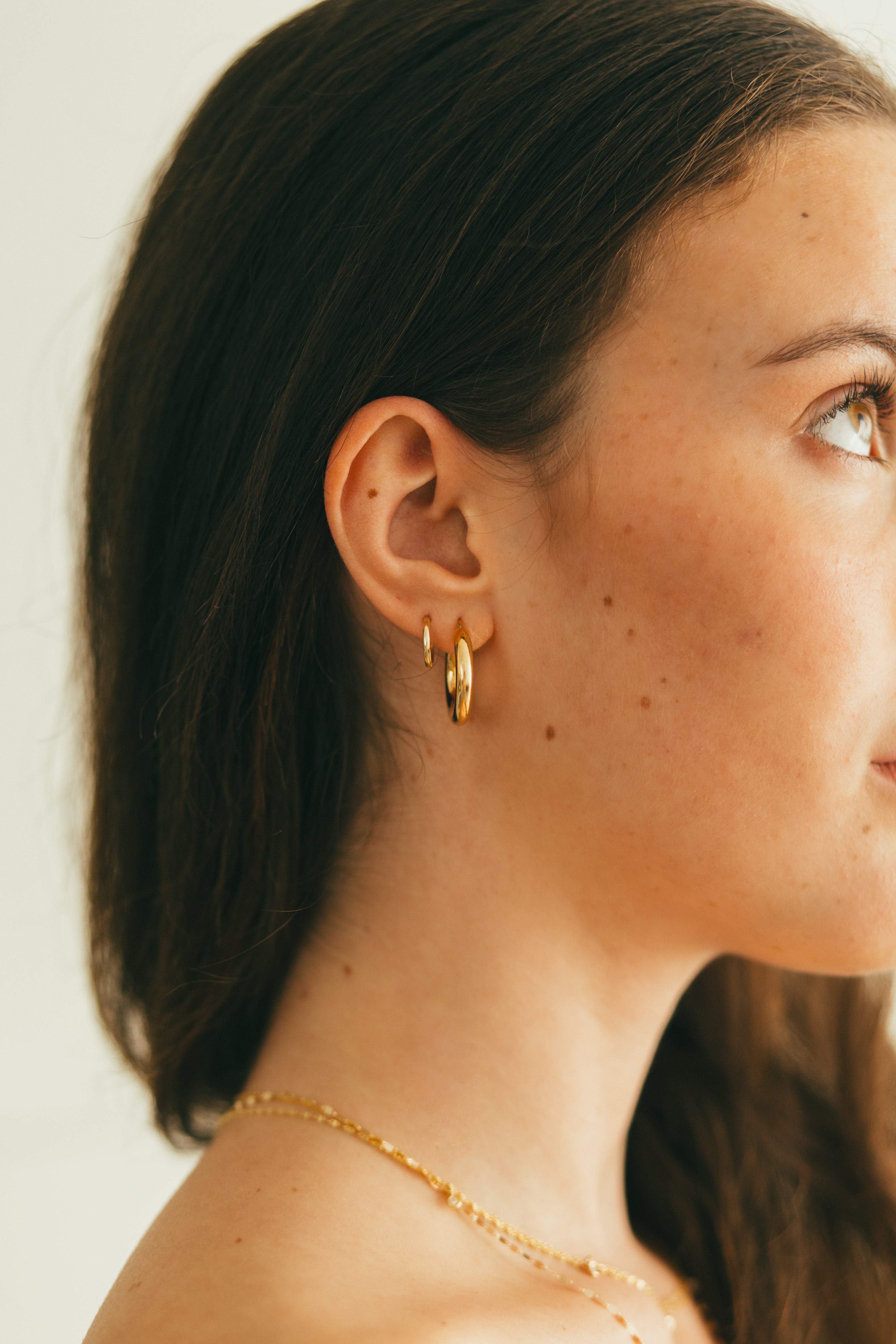 close up of girls ear wearing two gold hoops