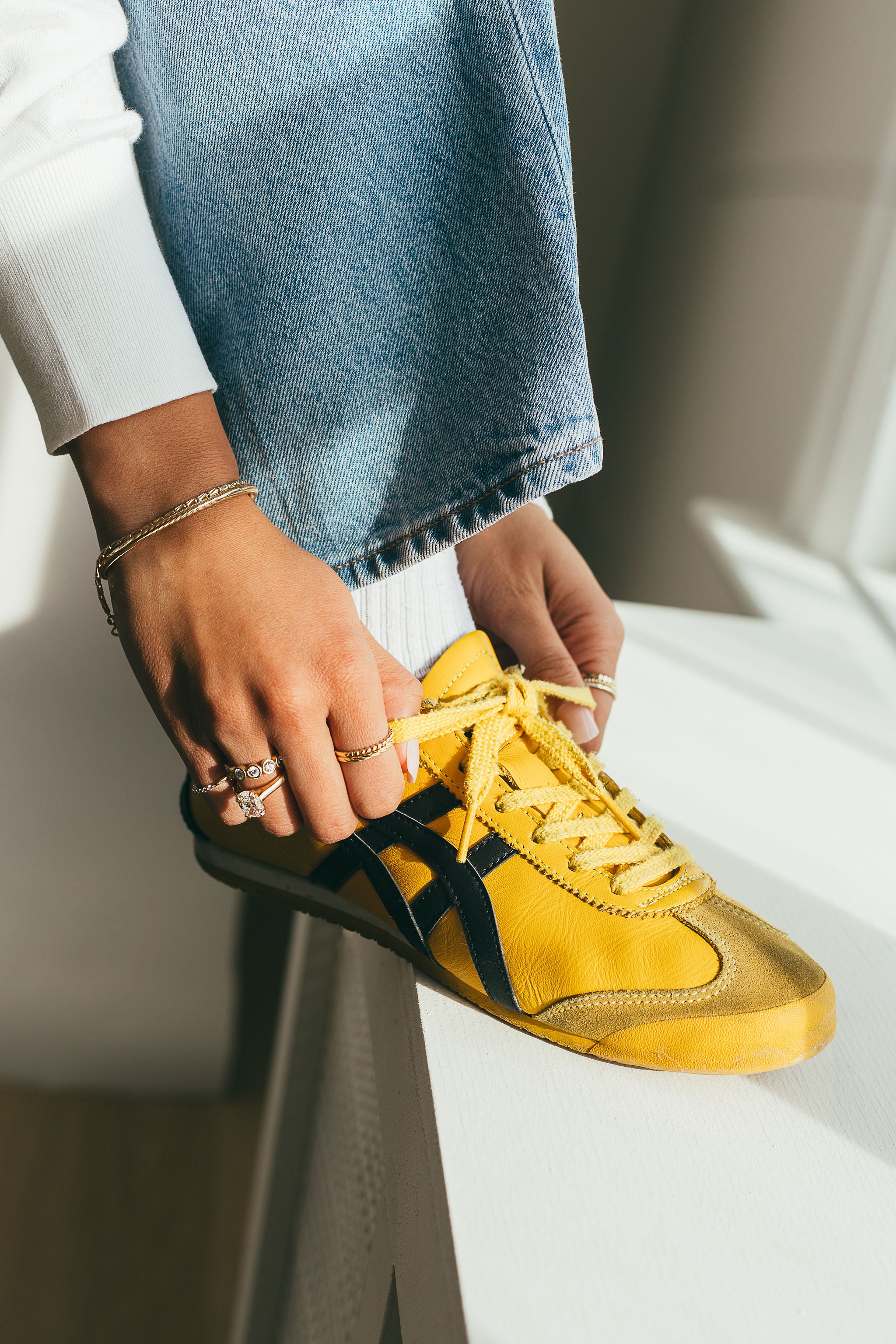 Yellow sneaker with black accents being worn by a person with diamond engagement ring and gold rings
