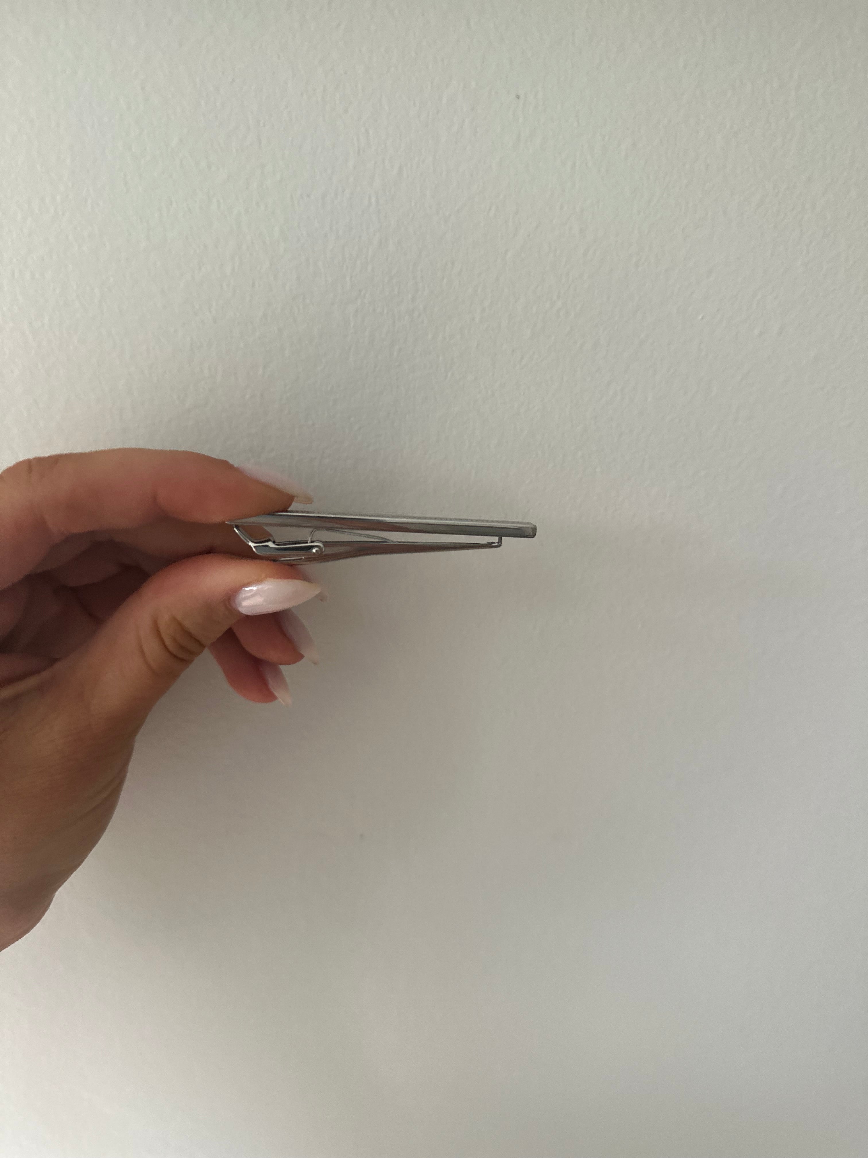 A side profile of a sterling silver bordered tie bar held between fingers against a neutral background.