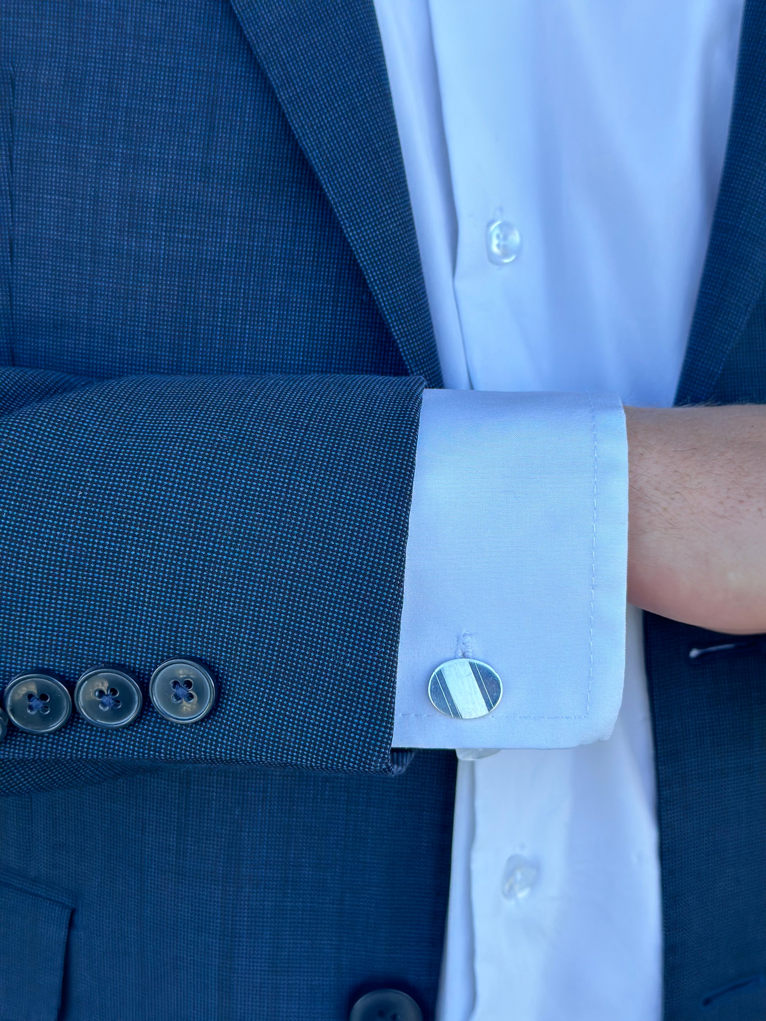 A sterling silver oval cufflink worn on the cuff of a man's dress shirt with a blue suit jacket.