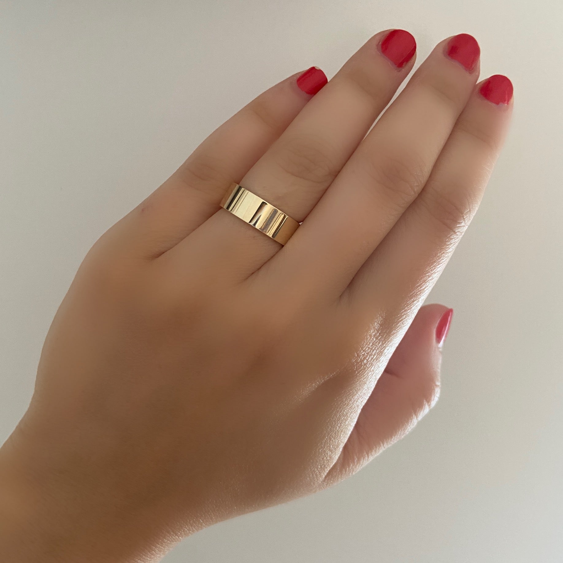 A close up of a person's hand wearing a single gold wide flat cigar band on a netural background.