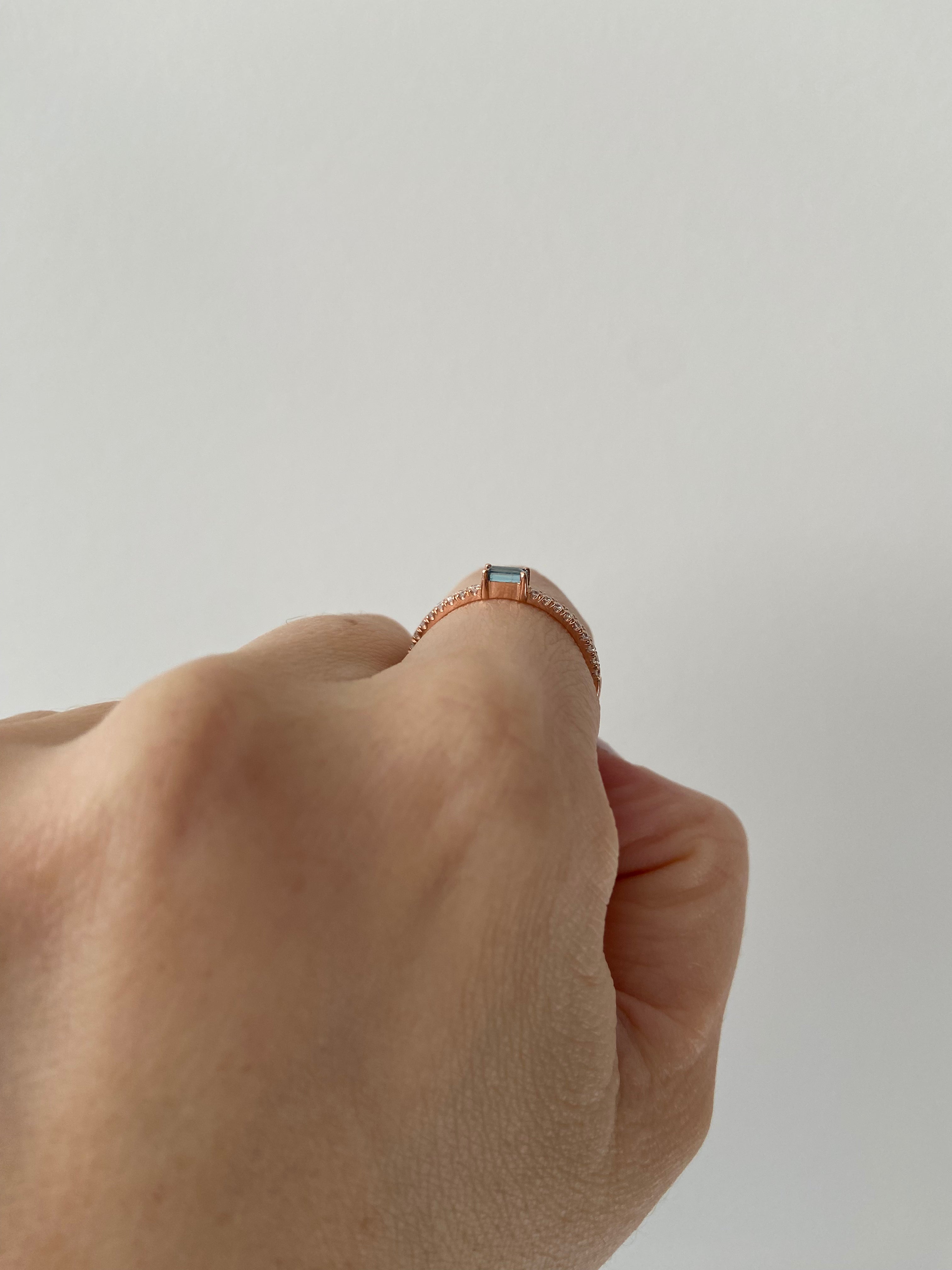 Side view of a hand wearing a baguette birthstone and diamond ring on a neutral background.