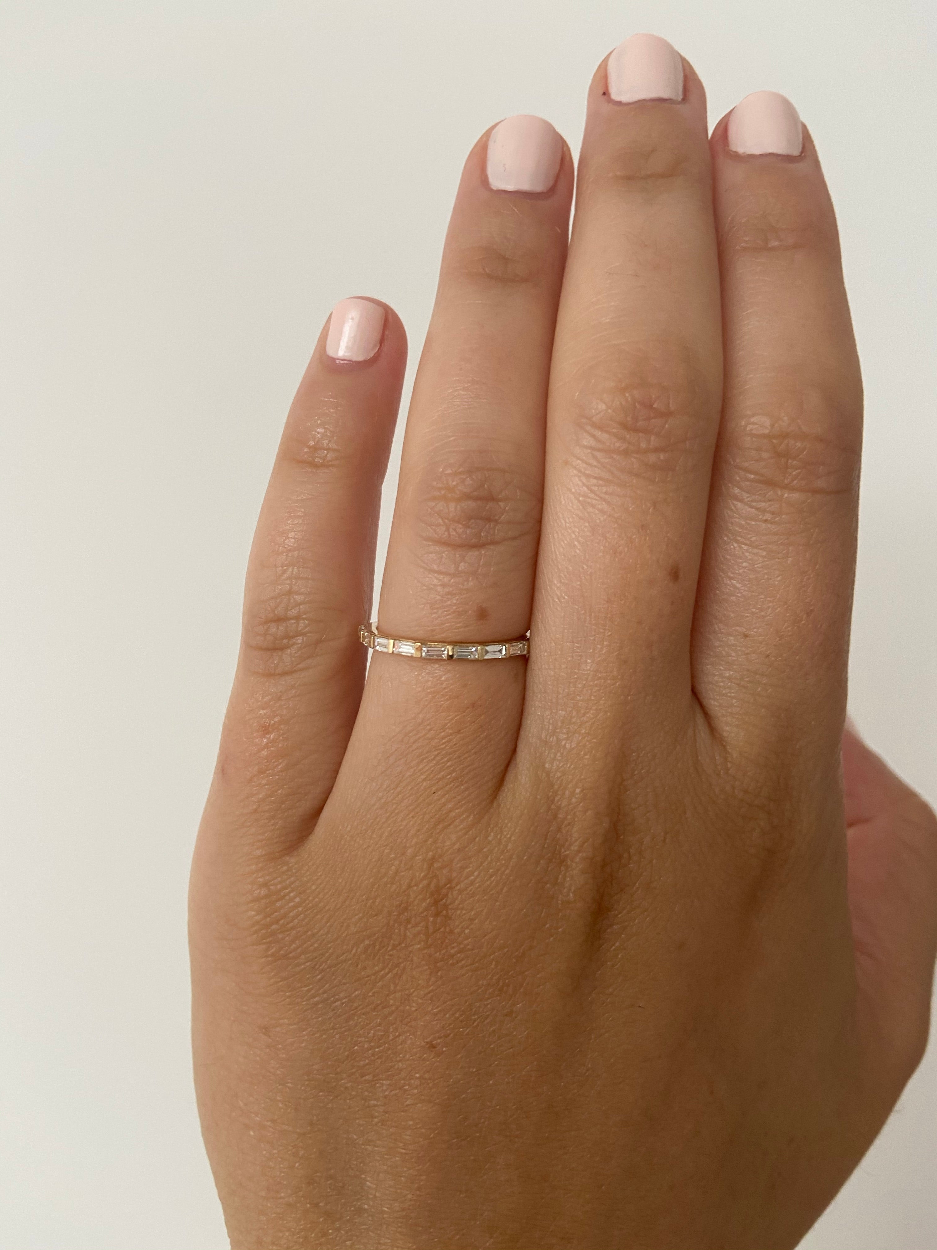 A woman's hand wearing a yellow gold diamond baguette ring on her index finger, on a neutral background.