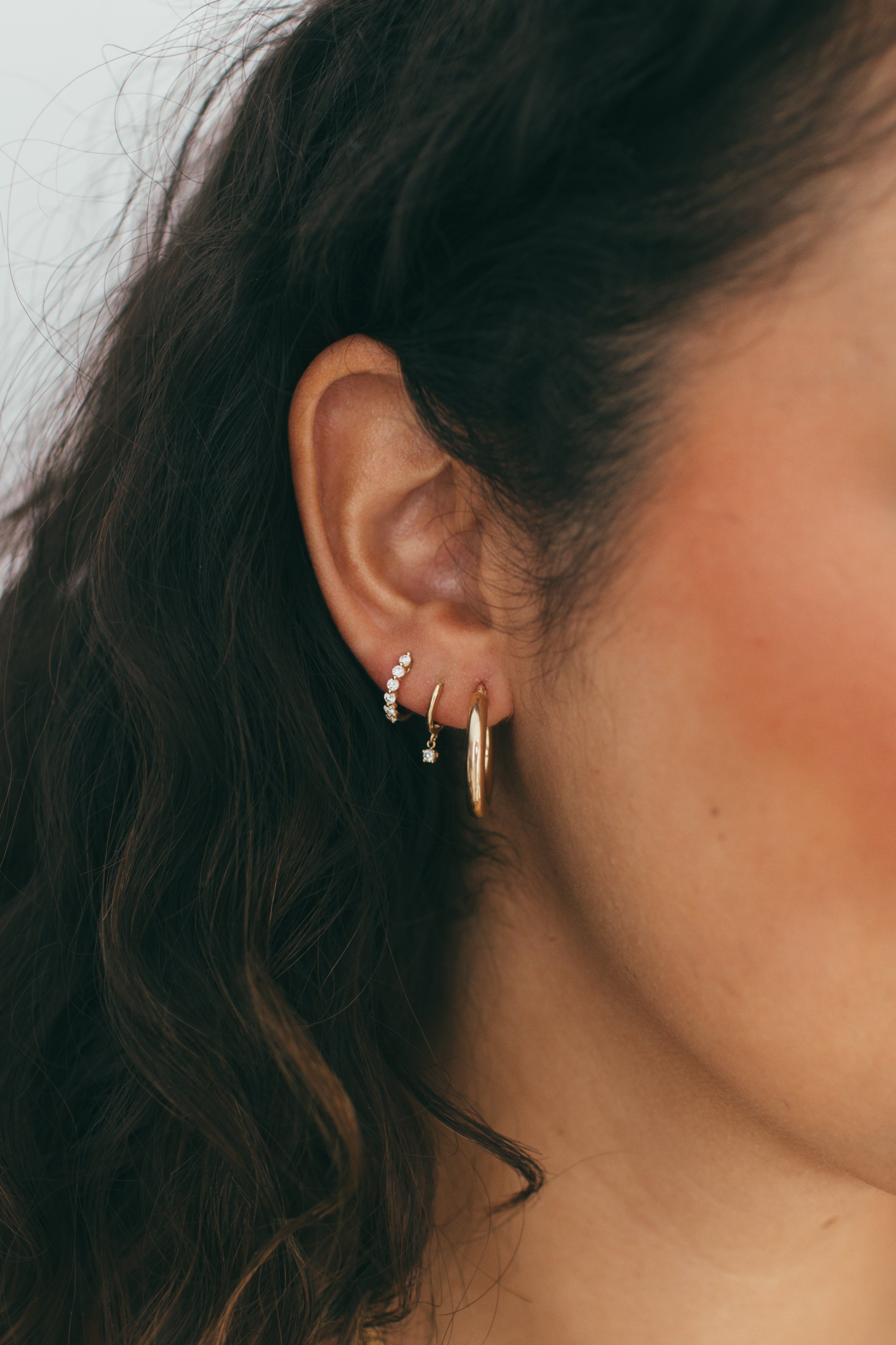 close up of ear wearing stack of gold hoops and diamond huggies