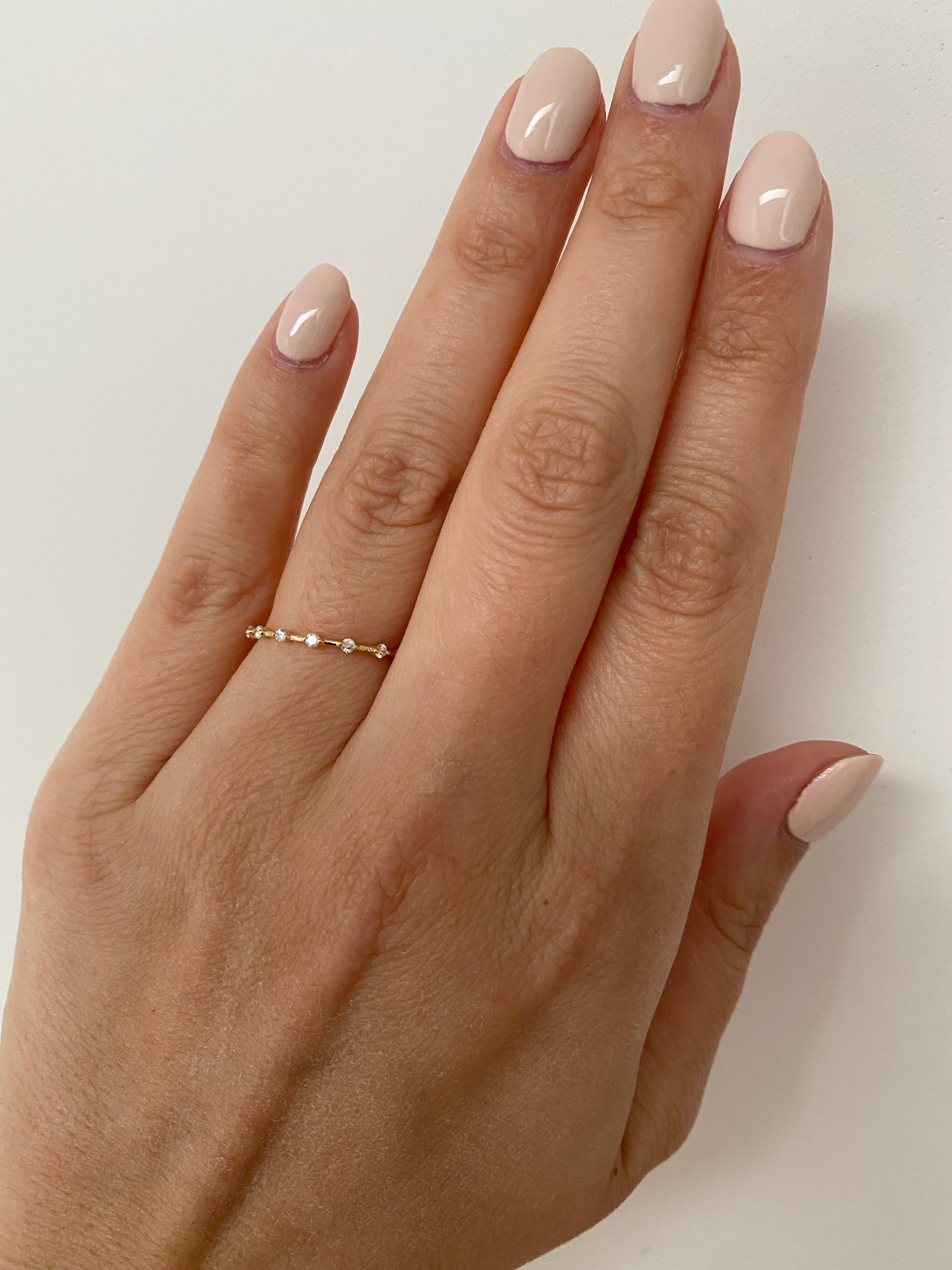 A hand wearing a single gold spaced diamond ring with a yellow gold band on a neutral background.