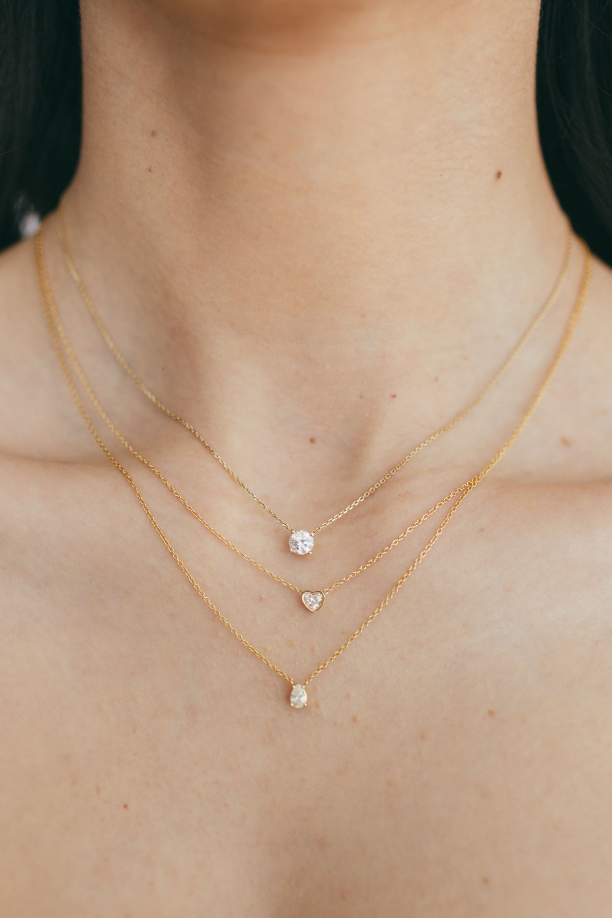 a stack of three diamond necklaces including a round diamond, heart diamond, and pear diamond