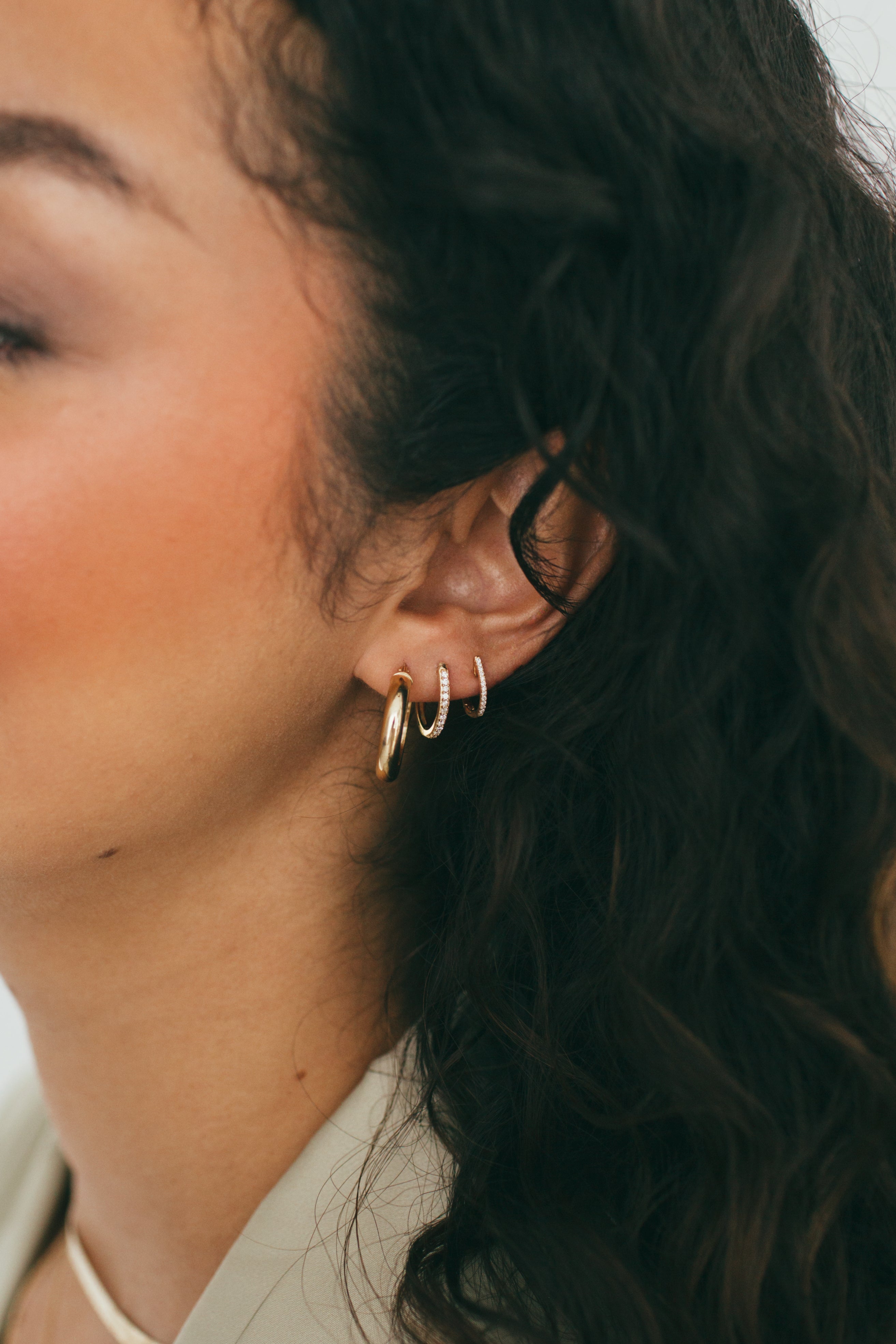 close up of girls ear wearing gold hoops, diamond hoops, and diamond huggies