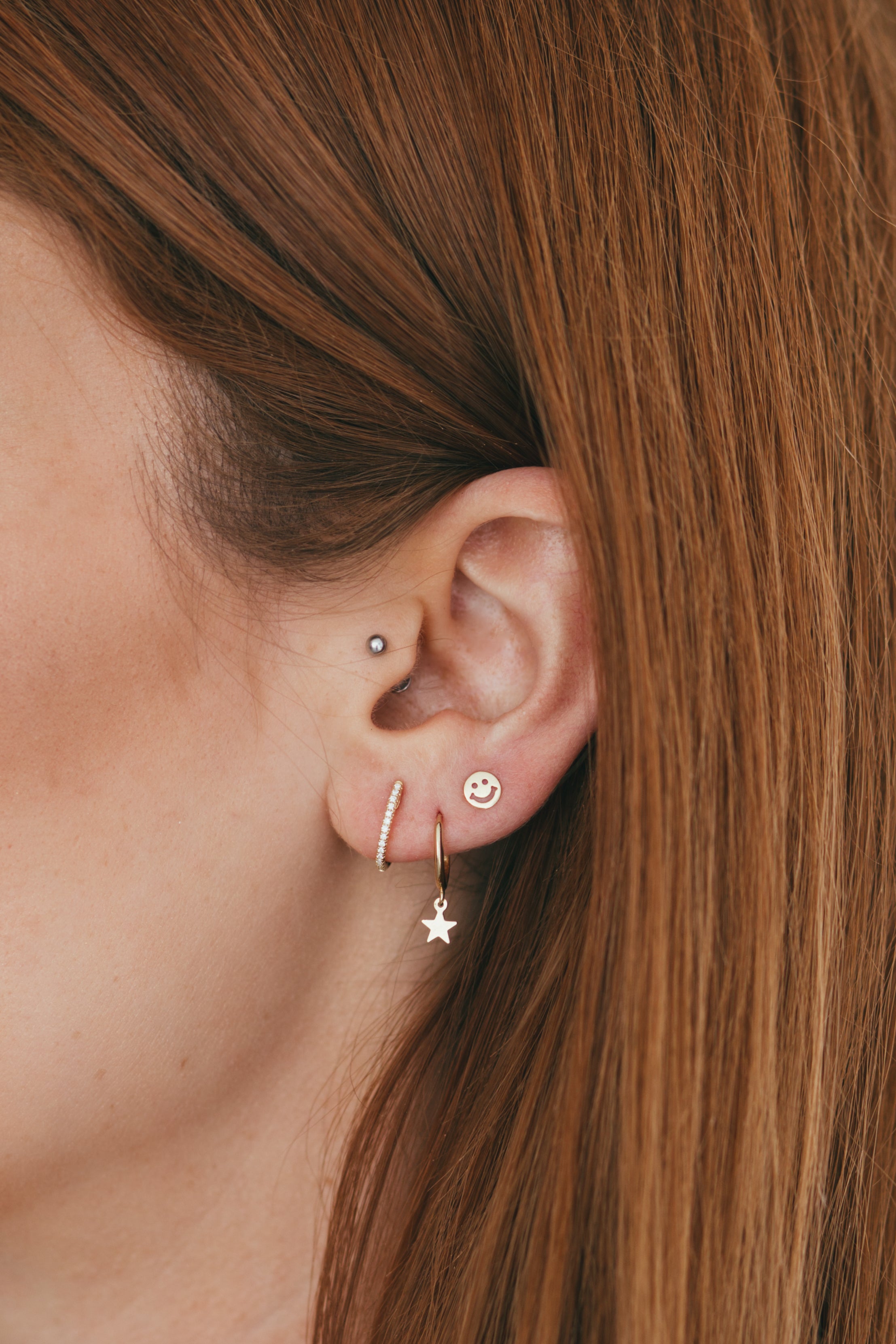 close up of an ear displaying diamond huggies, star huggies, and a smiley face stud