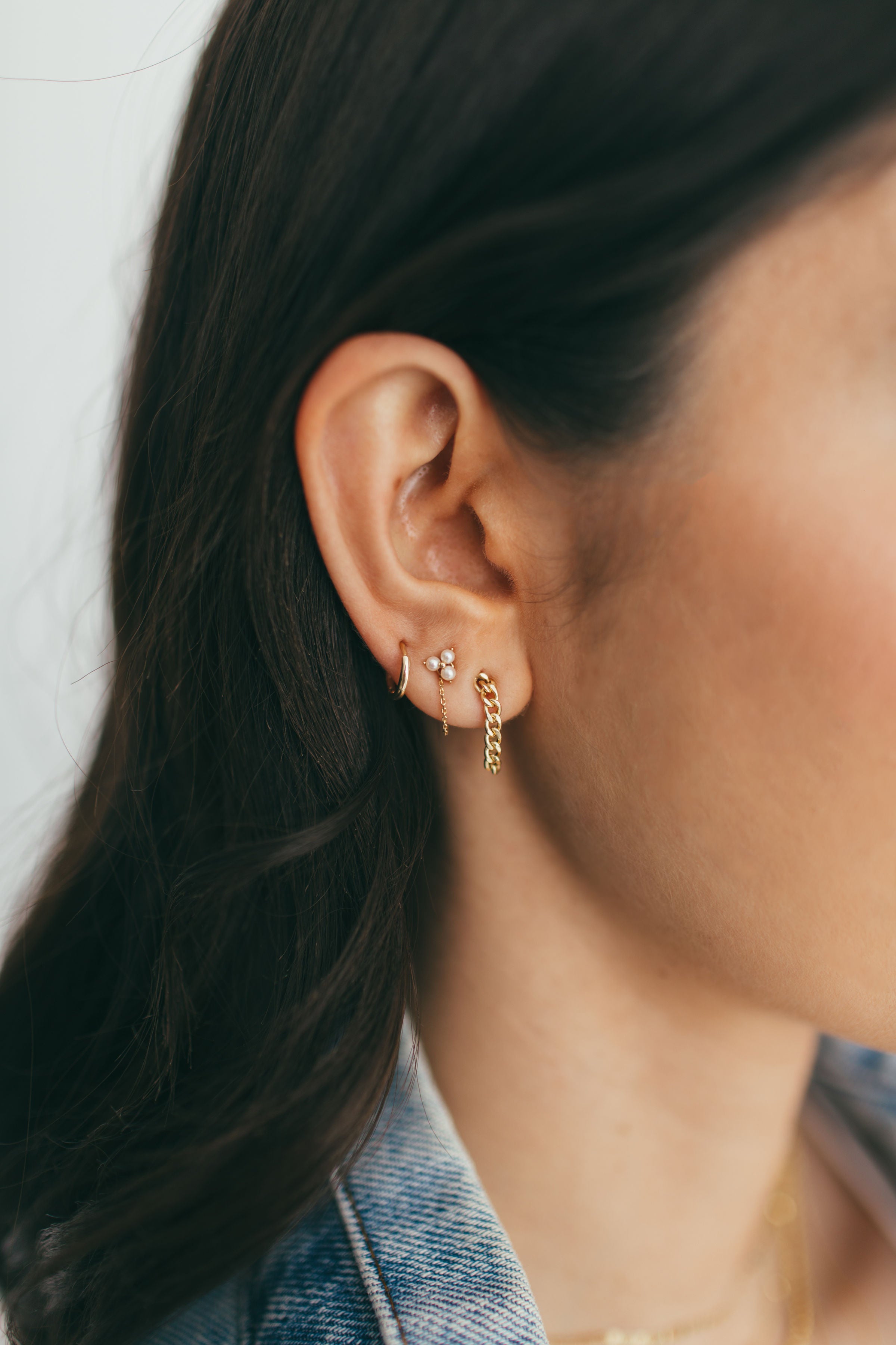 a girl wearing chain earrings, pearl trio studs, and mini gold huggies