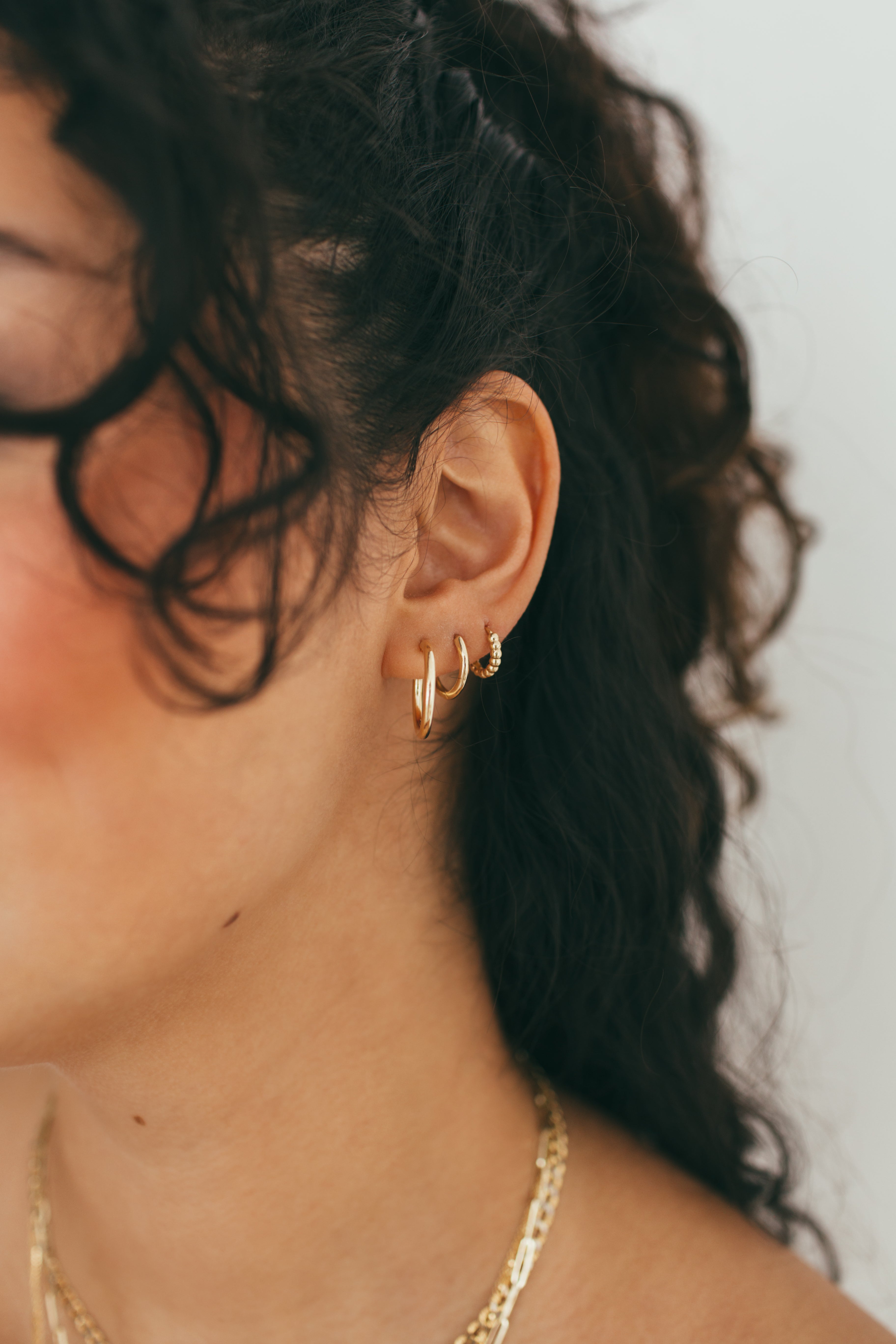 close up of girls ear wearing a gold earring stack of hoops