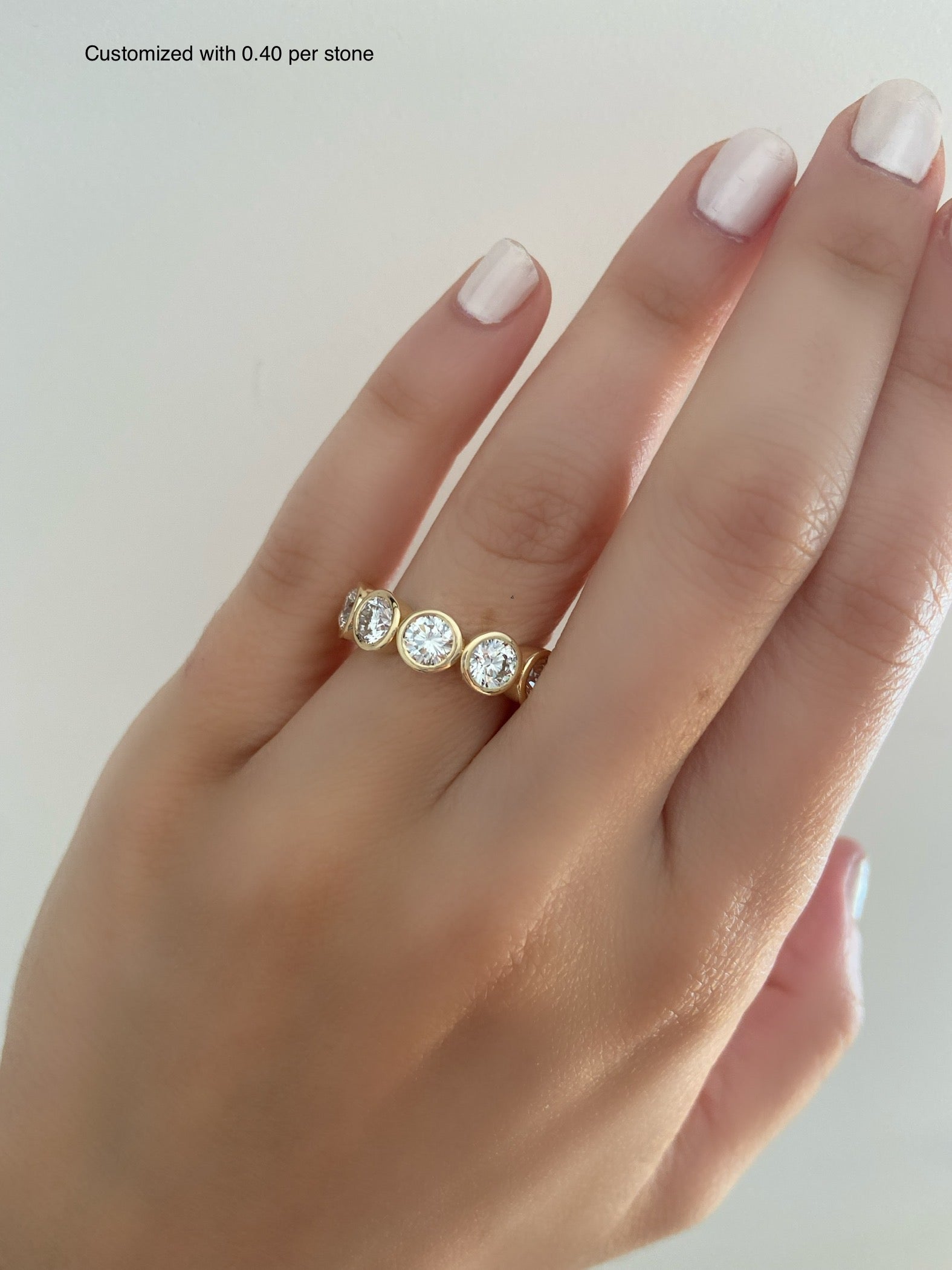 A close up of a person's hand wearing a diamond bezel ring with sparkling diamonds on a neutral background.
